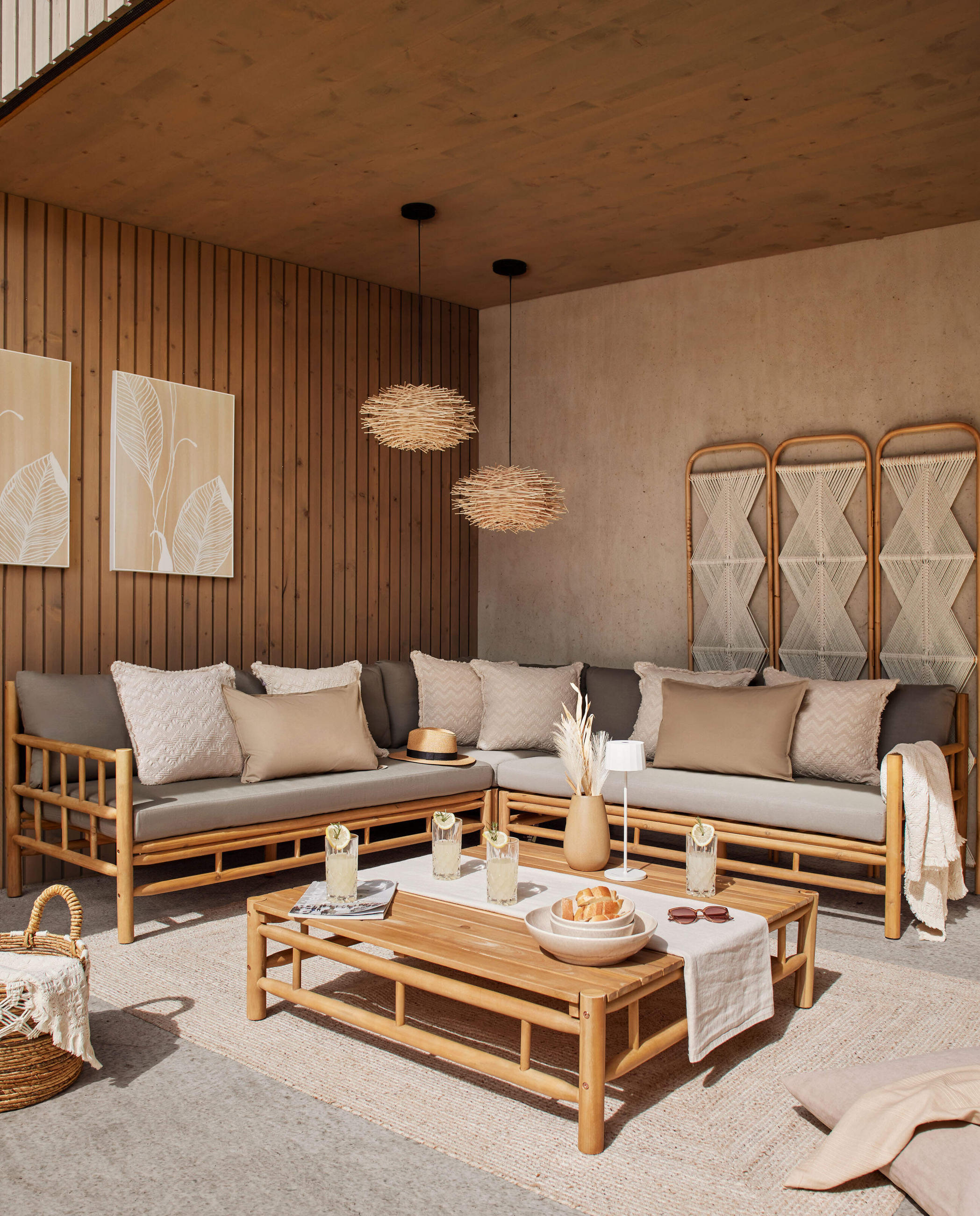 Outdoor-Sitzgruppe aus Bambus mit Ecksofa, Kissen und niedrigem Tisch, dekoriert mit Getränken und Wohnaccessoires