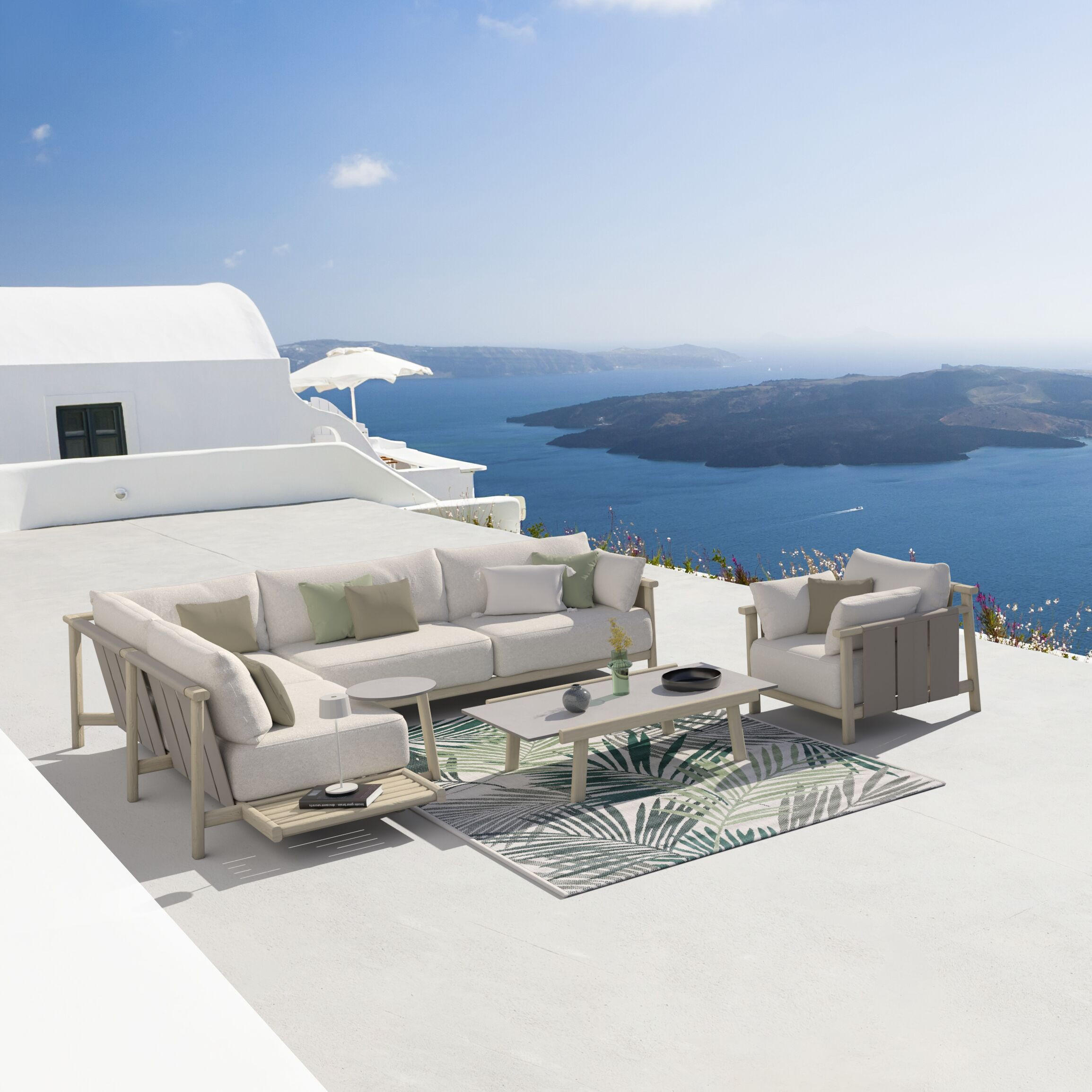 Helle Outdoor-Lounge mit Sofa, Sessel und Couchtisch auf weißer Terrasse, dahinter tiefblaues Meer und Inseln.