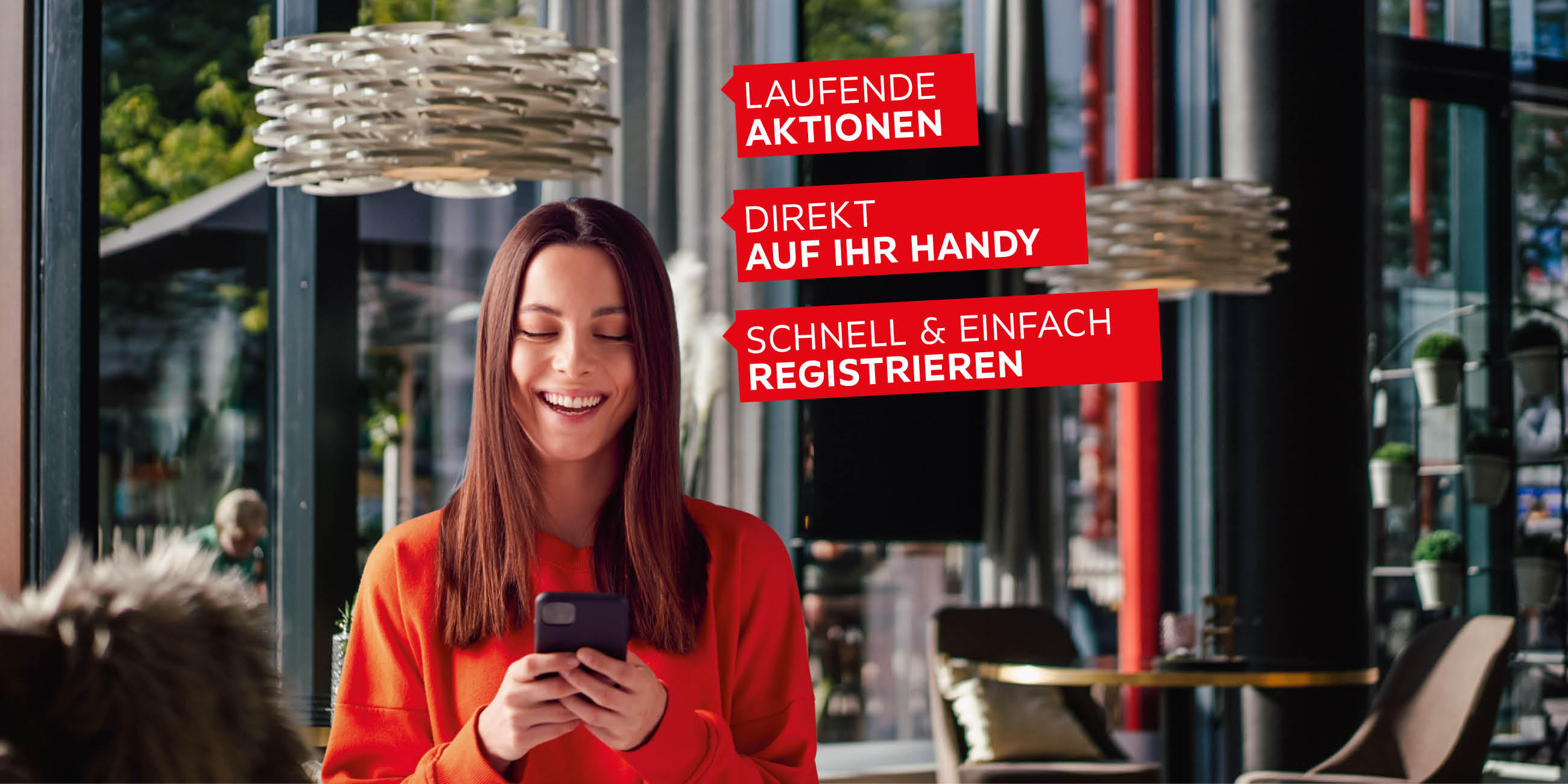 Lächelnde Frau mit Smartphone im Café, Text: „LAUFENDE AKTIONEN“, „DIREKT AUF IHR HANDY“, „SCHNELL & EINFACH REGISTRIEREN“