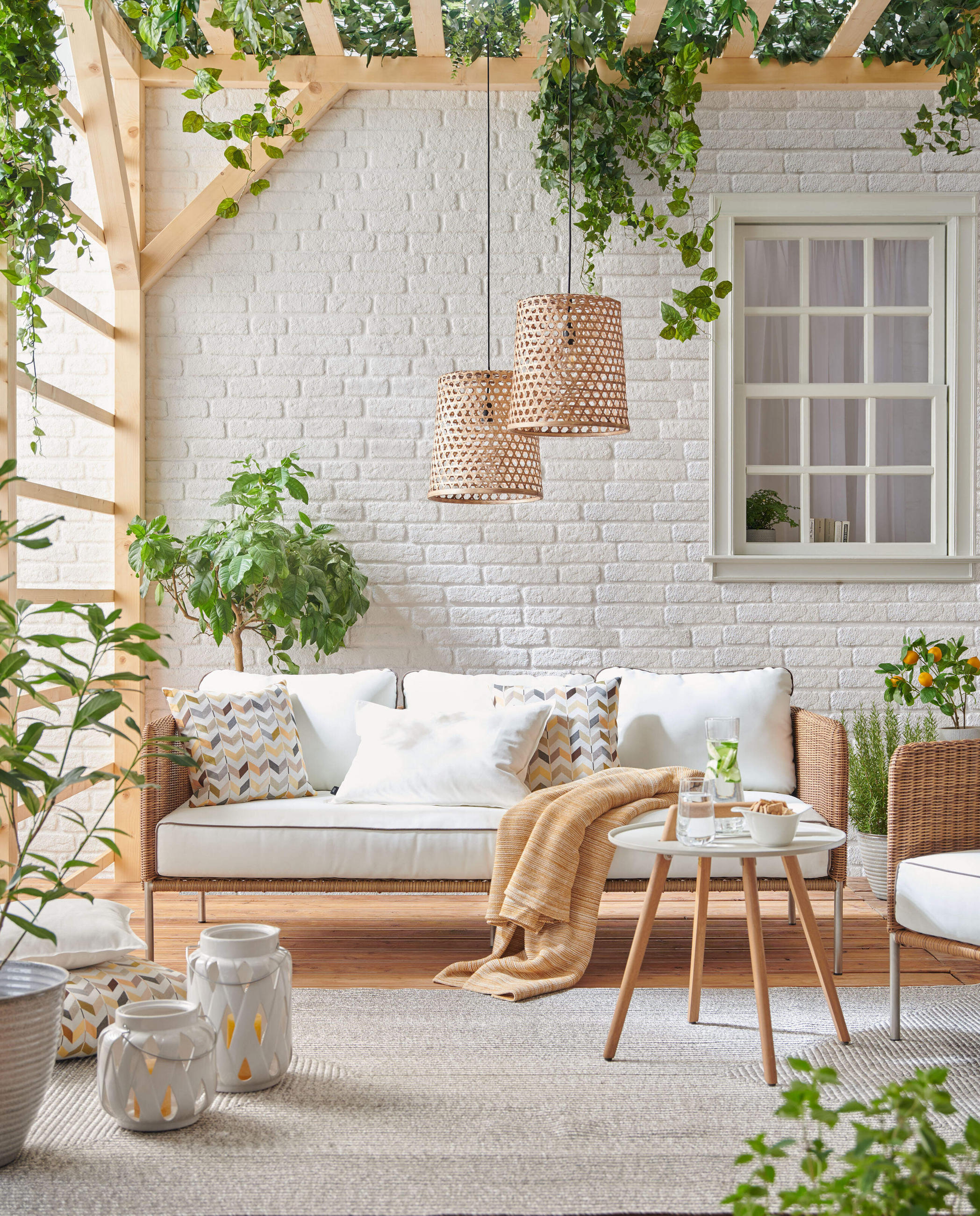 Terrassenlounge mit Rattansofa, hellen Polstern, Beistelltisch und hängenden Korblampen unter Pergola