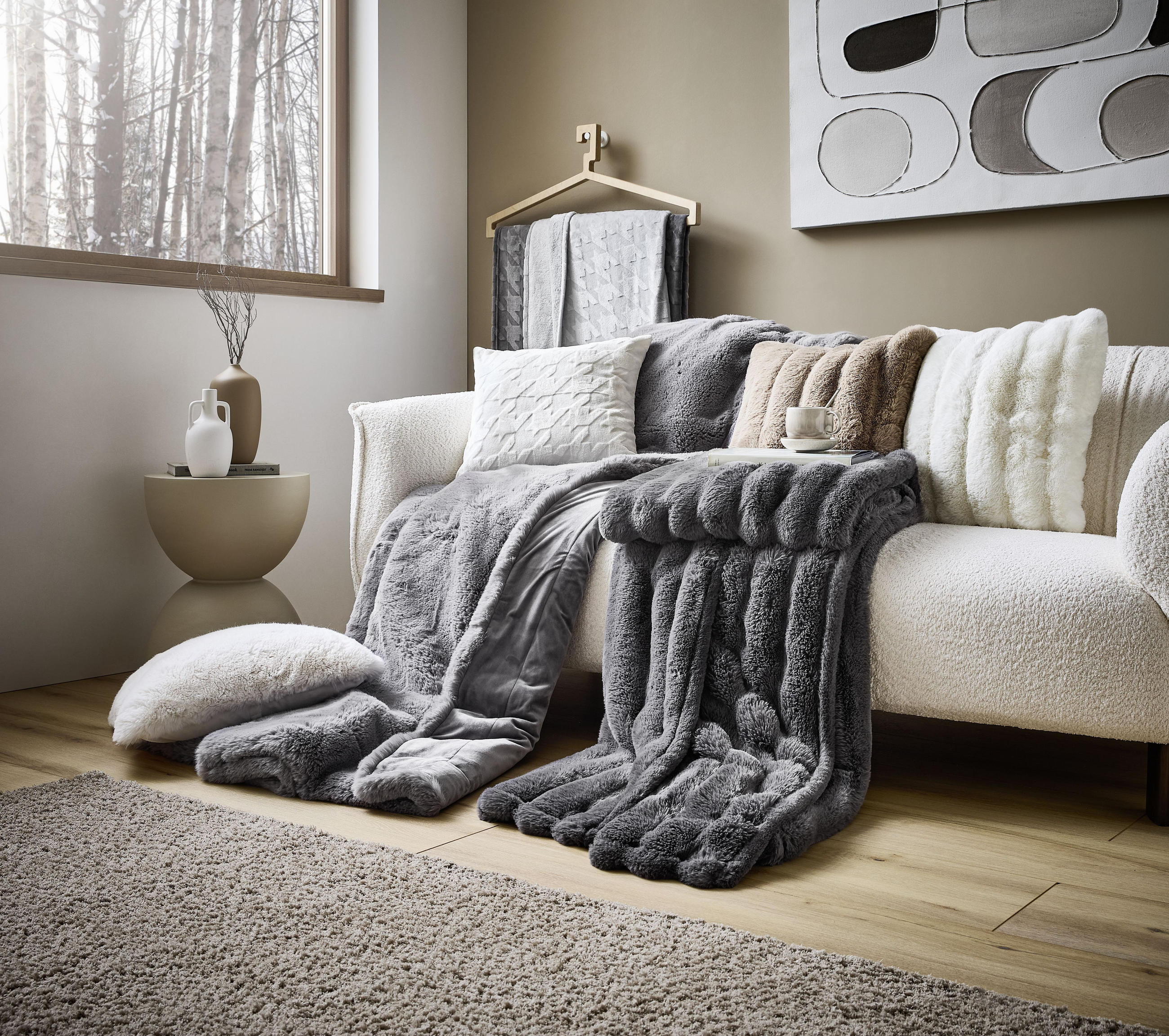 Hřejivé deky a polštáře na sedačce v krémové barvě