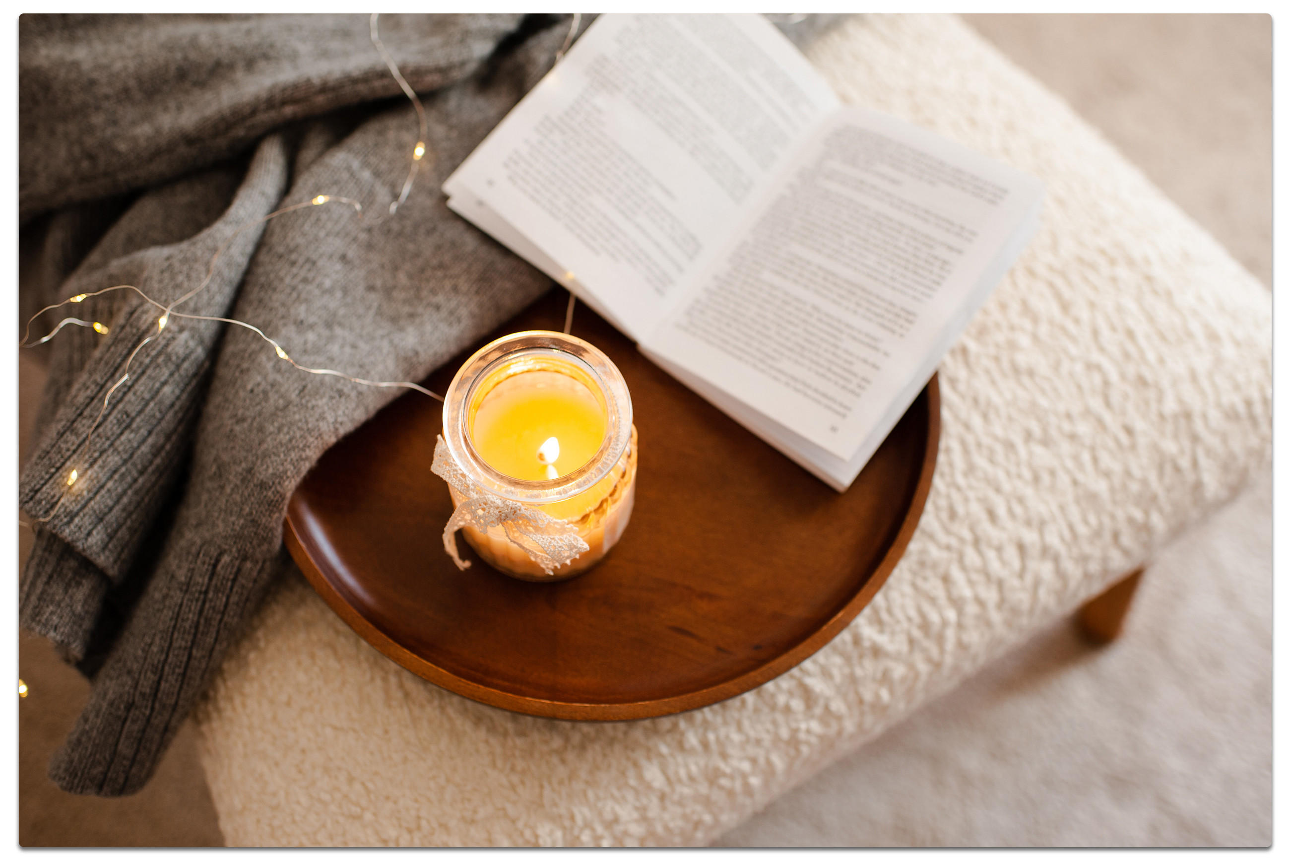Eine Kerze und ein Buch auf einem Holztablett, die eine gemütliche und einladende Atmosphäre schaffen