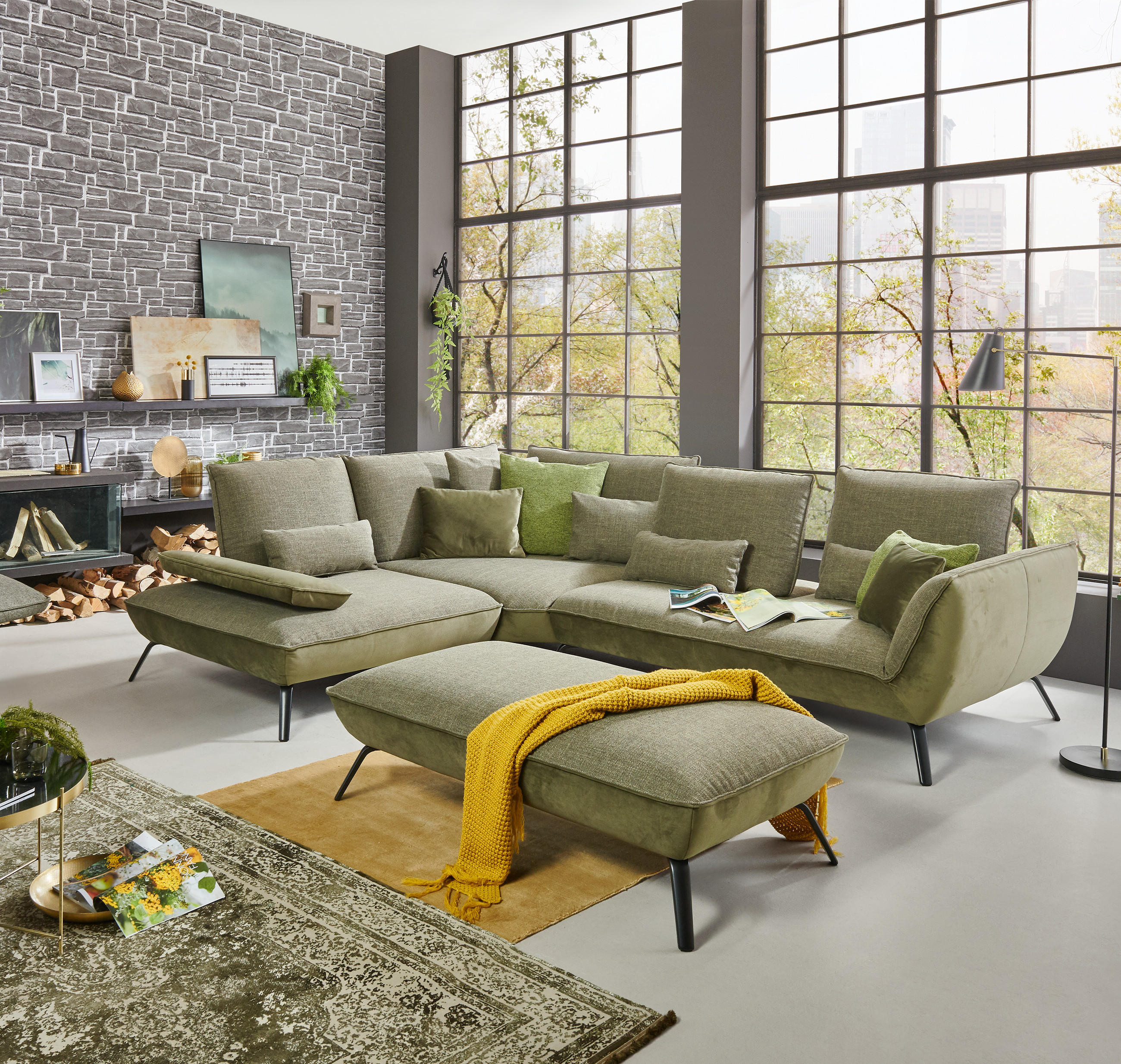 Modernes Wohnzimmer mit grünem Ecksofa, passendem Hocker, grauem Sessel, Kamin und großen Fenstern.