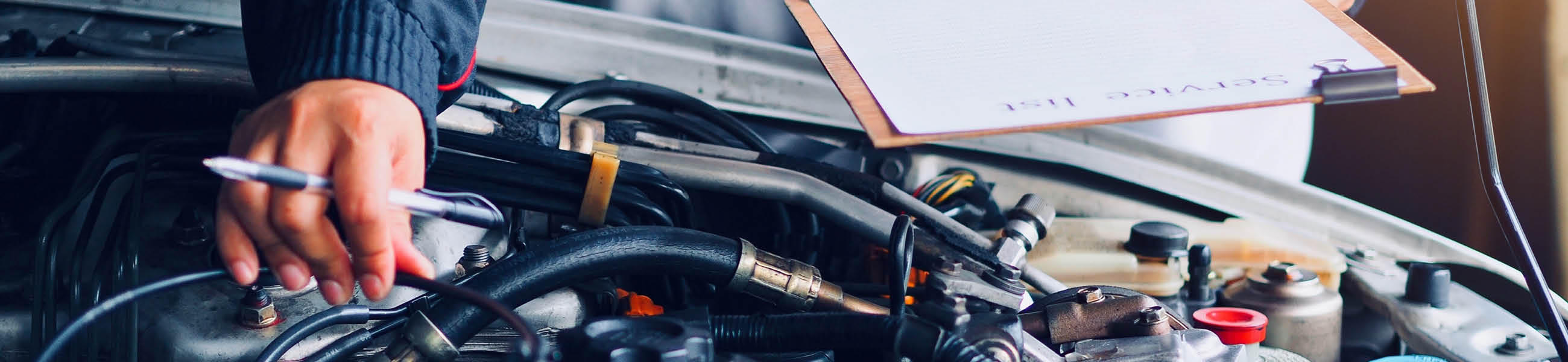 Nahaufnahme einer Hand, die an einem Motor arbeitet, während eine andere Hand einen Stift hält und Notizen auf einem Clipboard macht. Der Kontext deutet auf einen Heimwerker-Ratgeber hin.