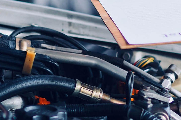 Hand eines Heimwerkers, der an einem Motor arbeitet, während er Notizen auf einem Clipboard macht.