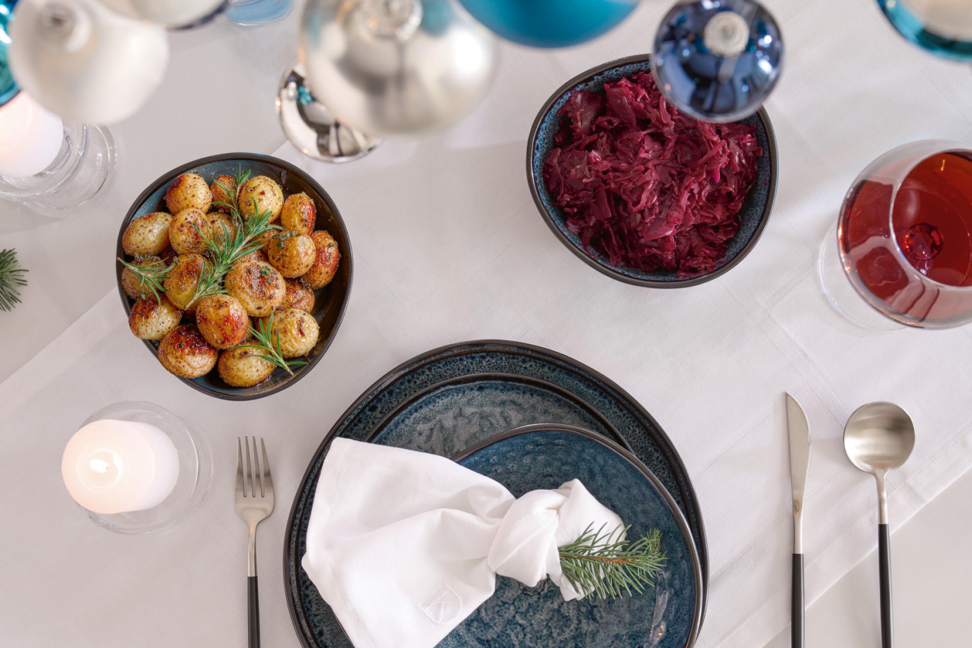 Gedeckter weißer Esstisch mit schwarzem Service; Tischdeko Weihnachtskranz mit blauen & weißen Kugeln