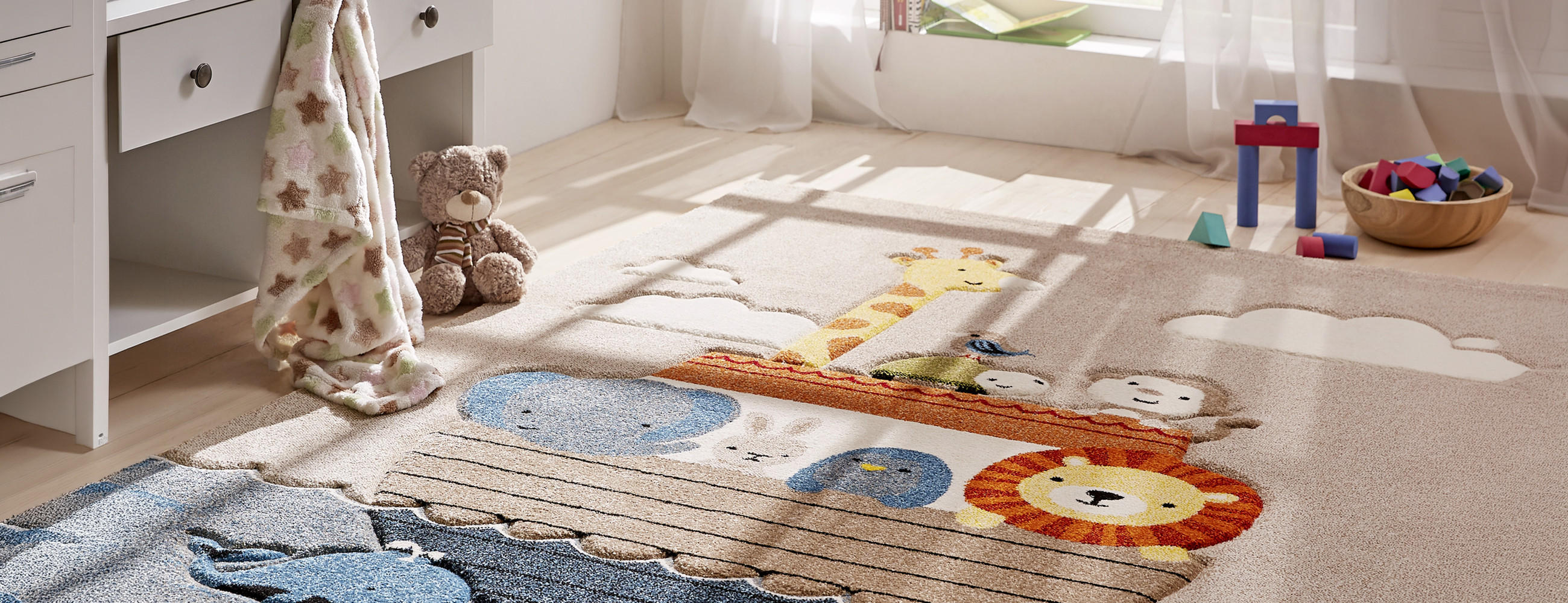 Kinderzimmer mit Teppich, der Tiere wie Elefant, Giraffe, Affe und Löwe zeigt, und Spielzeug im Hintergrund.