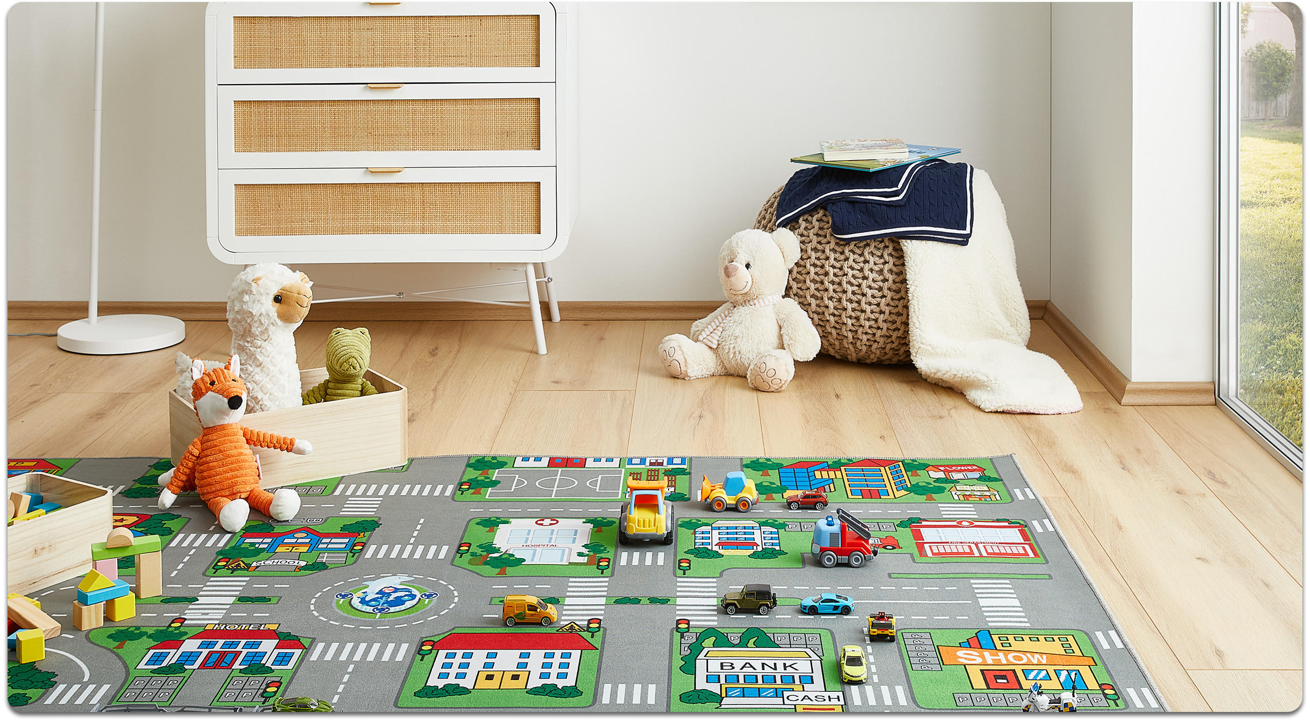 Kinderzimmer mit Spielteppich in Straßenmuster, mehreren Spielzeugautos, Kuscheltieren und einem gepolsterten Sitzhocker mit Decken.