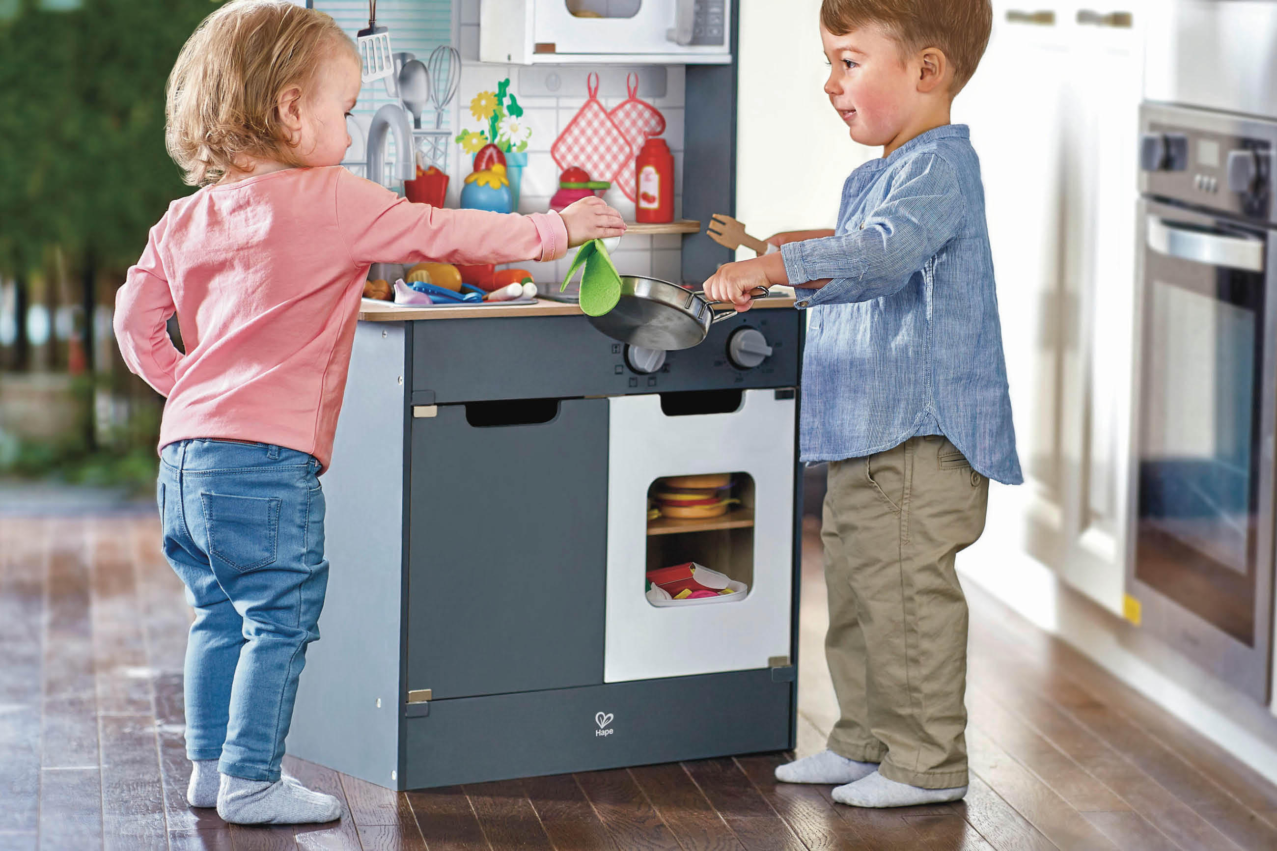 Zwei Kinder spielen fröhlich mit einem Spielküchen-Set und tun so, als würden sie kochen.