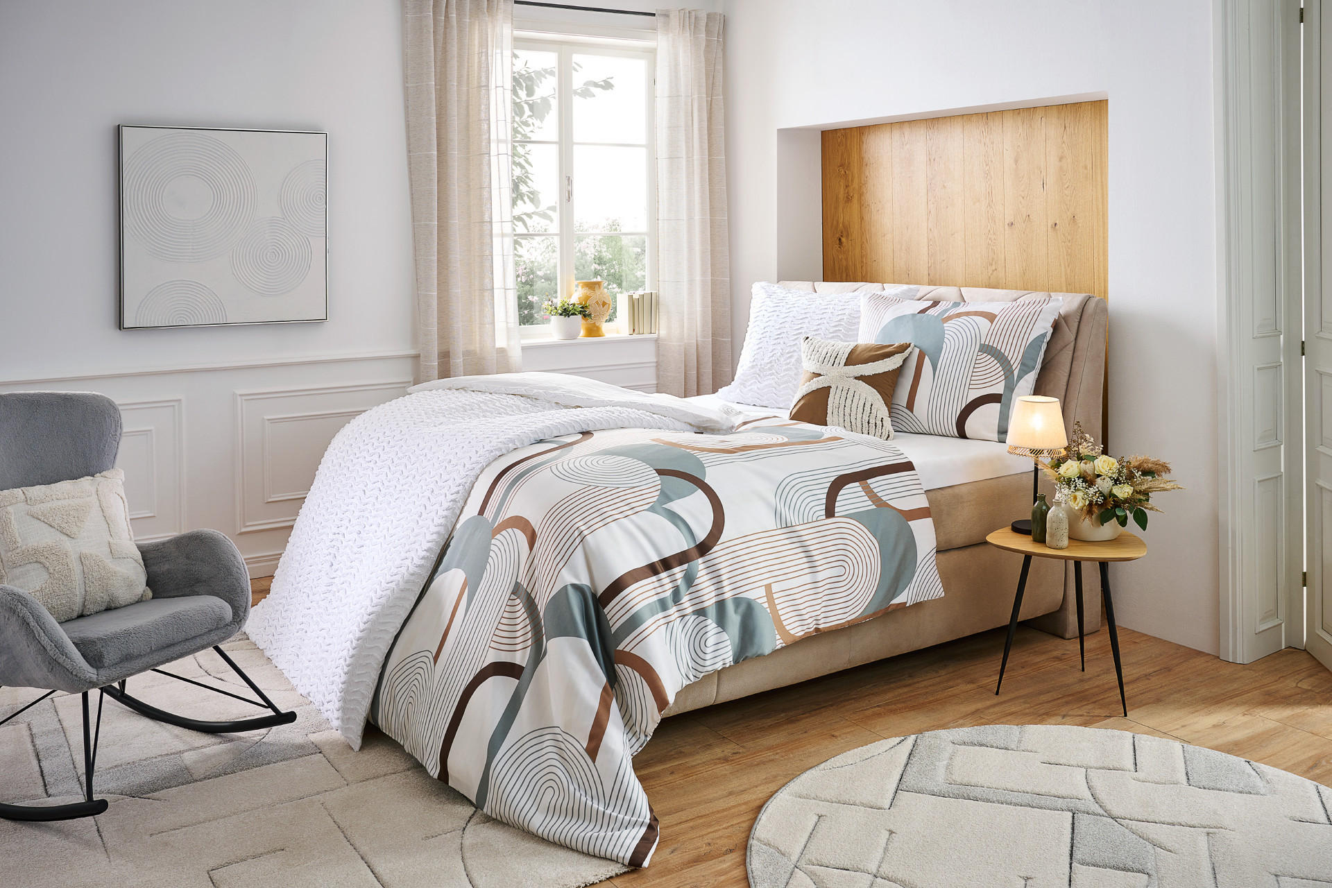 interior chic spálňa: bavlna, drevo, obliečky s geometrickým vzorom, sivé hojdacie kreslo