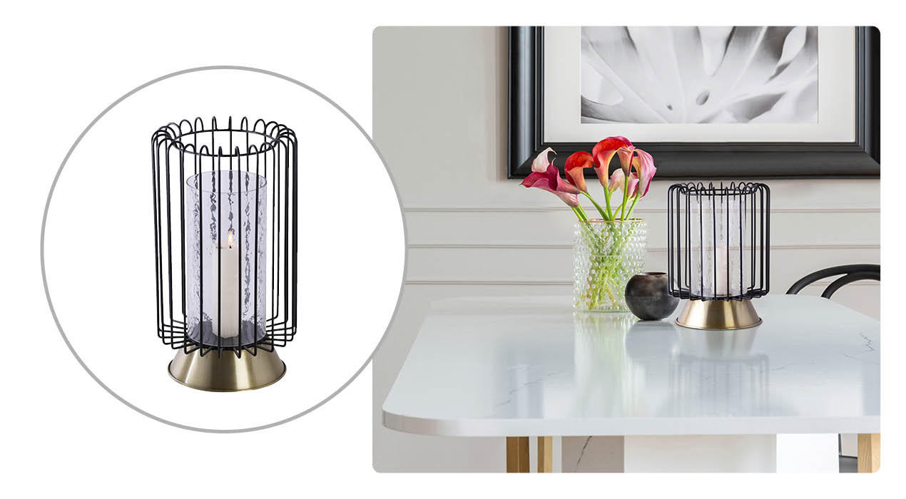  Moderner Kerzenhalter mit schwarzem Metallgitter, transparentem Glaszylinder und goldfarbenem Fuß; daneben eine Wohnszene, in der der Kerzenhalter auf einem weißen Tisch neben einer Vase mit farbigen Blumen steht.