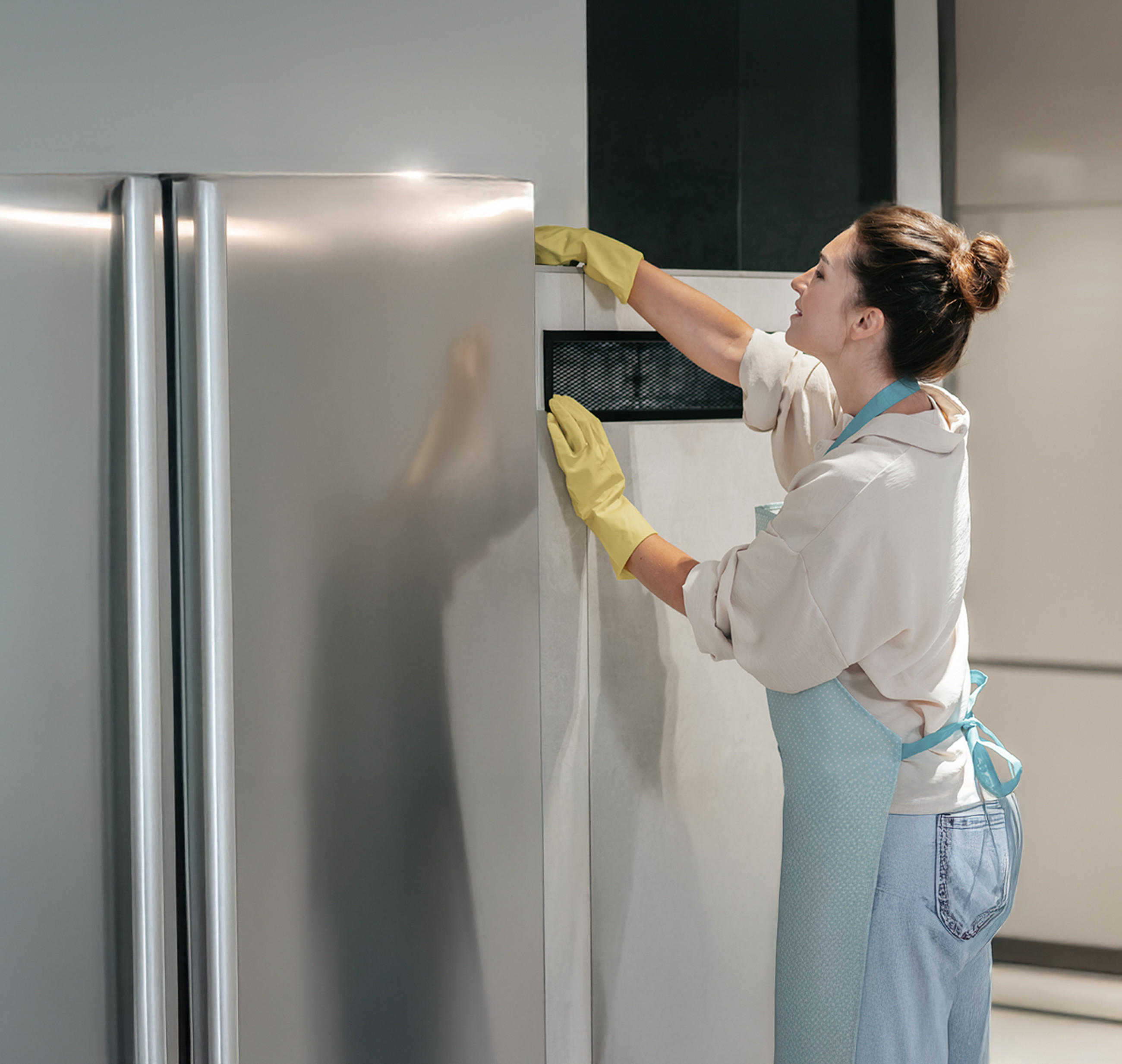 Eine Frau in Handschuhen und Schürze reinigt einen Kühlschrank von außen.