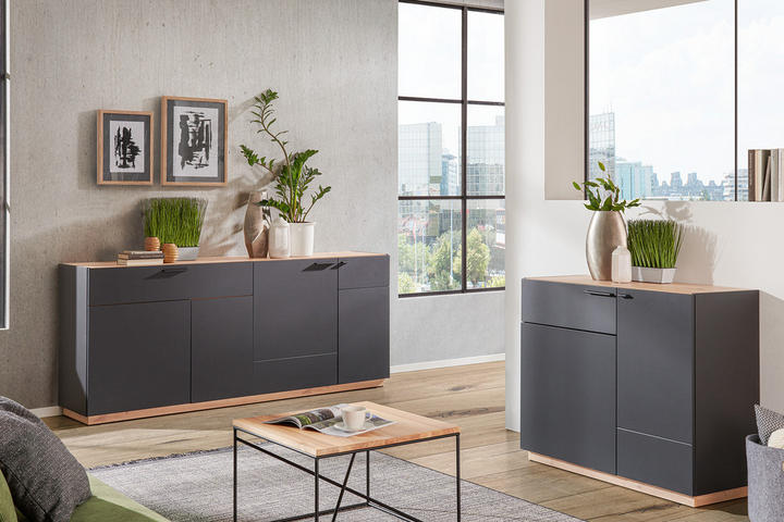 Moderný obývací priestor s tmavým nábytkom (tmavošedé komody) a s veľkými oknami s výhľadom na mesto.