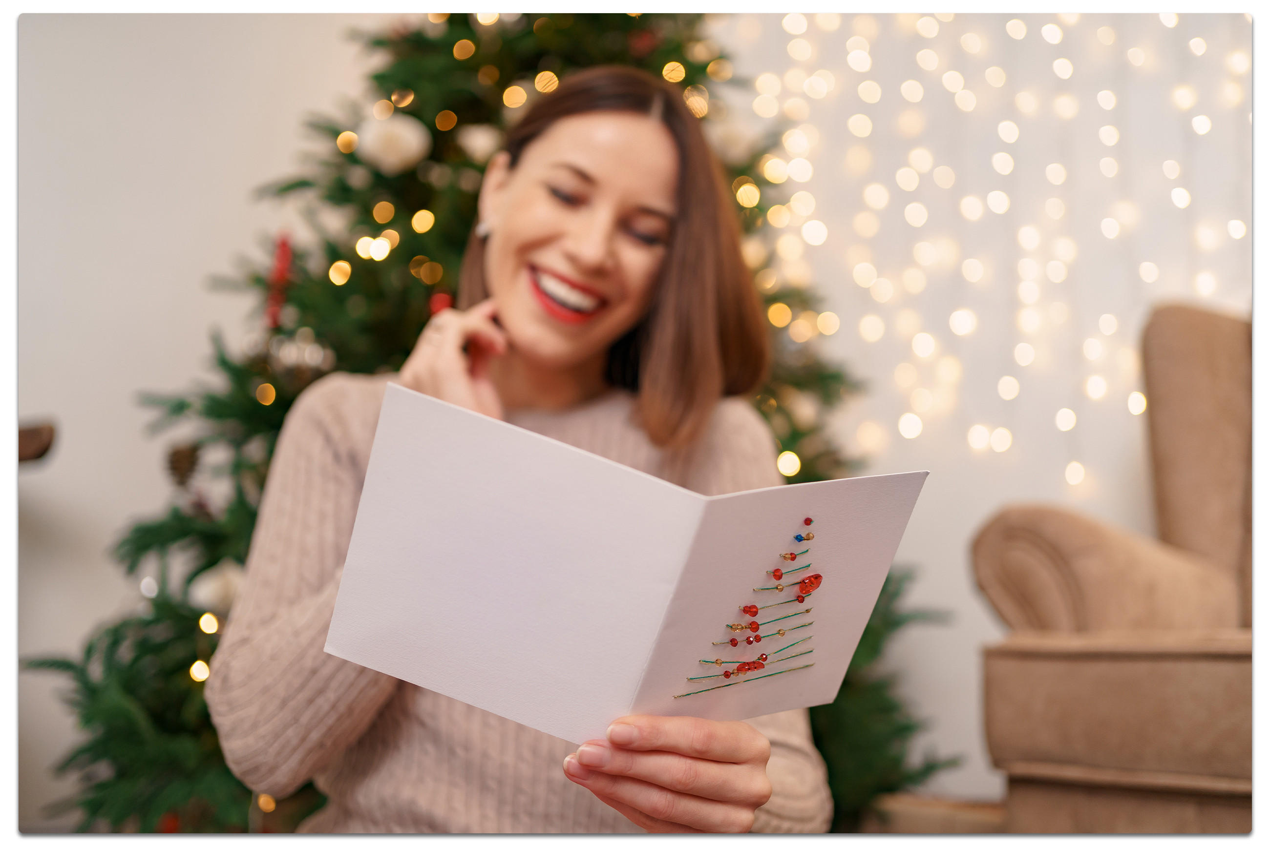 Eine lächelnde Frau hält eine Weihnachtskarte in der Hand und strahl Freude aus.