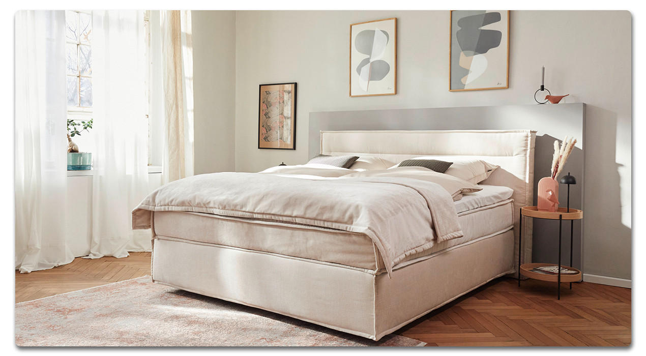 Bett in beige vor einer Wand in Pastelltönen