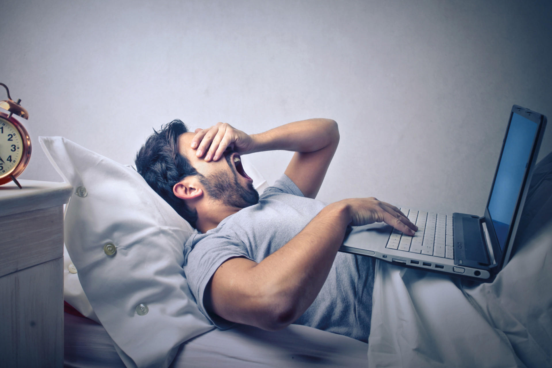 Mann im Bett mit Wecker am Nachttisch