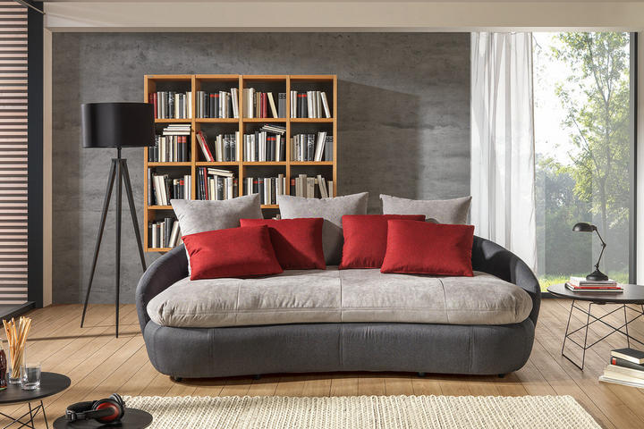 Moderná obývačka: šedá pohovka, drevená knižnica a betónová stena
