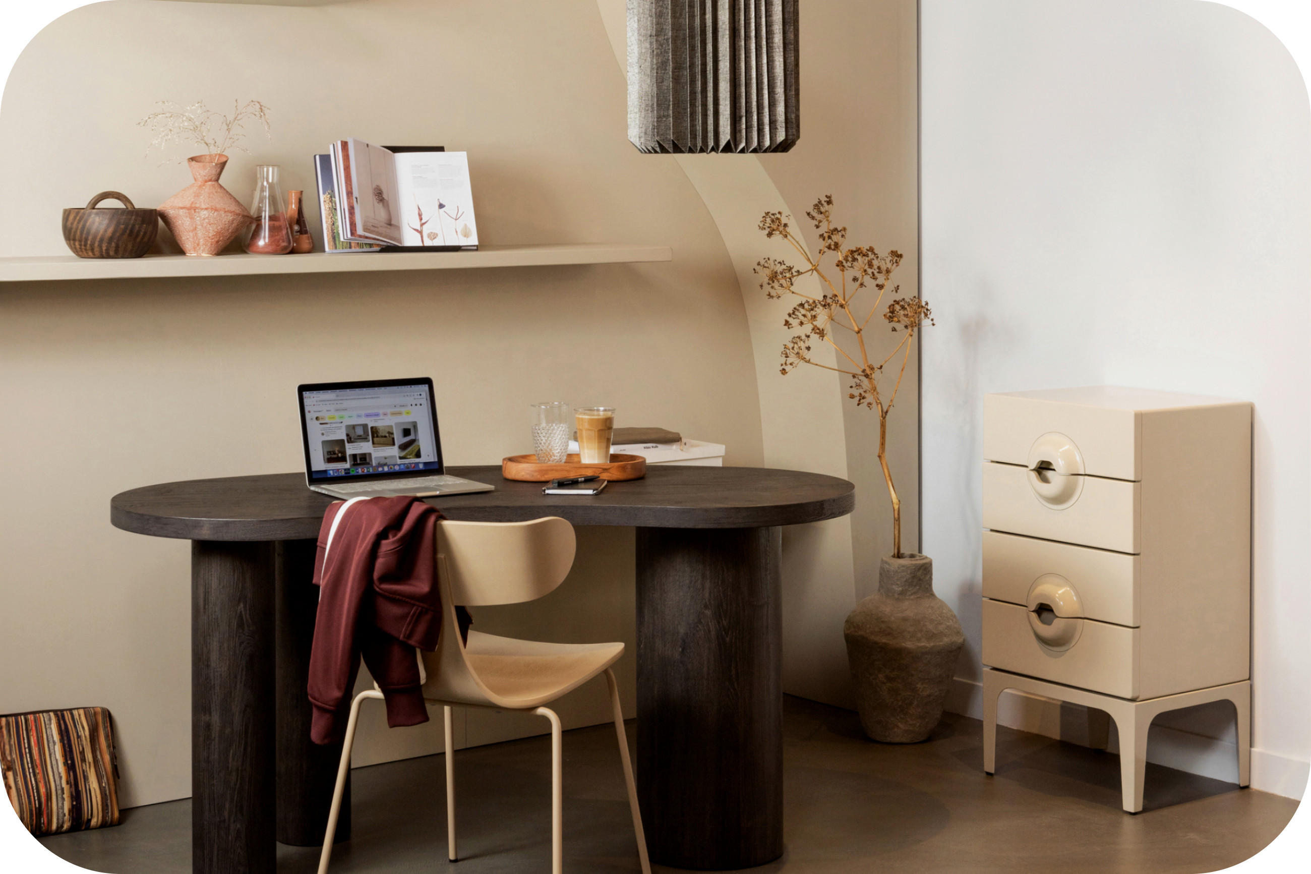 Homeoffice mit rundem Tisch, Laptop, Regalboard, Vase und heller Kommode.