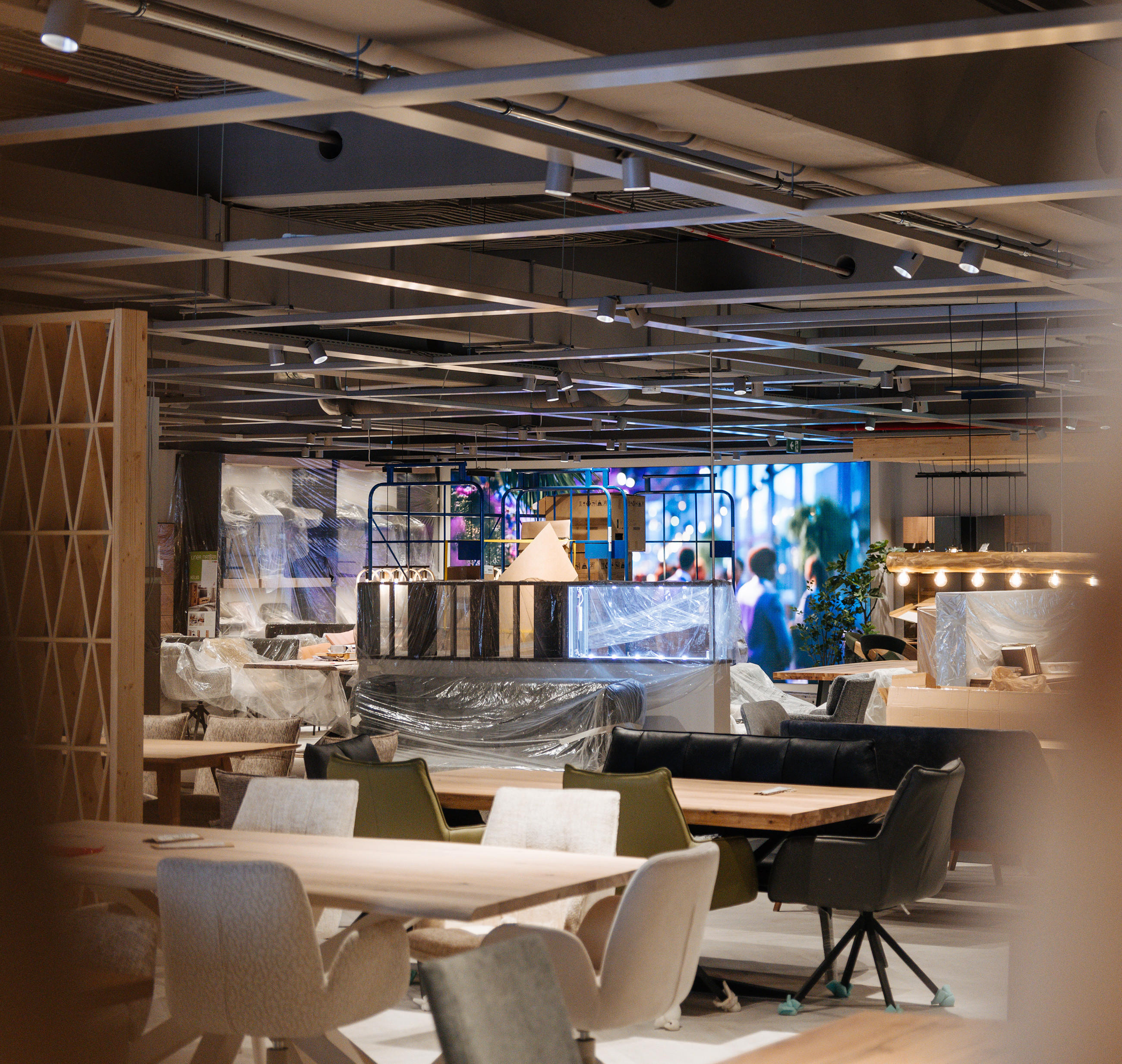 Blick in eine modern eingerichtete Ausstellungsfläche mit verpackten Möbeln, dekorativer Beleuchtung und Raumteilern während eines Aufbaus oder Umbaus.