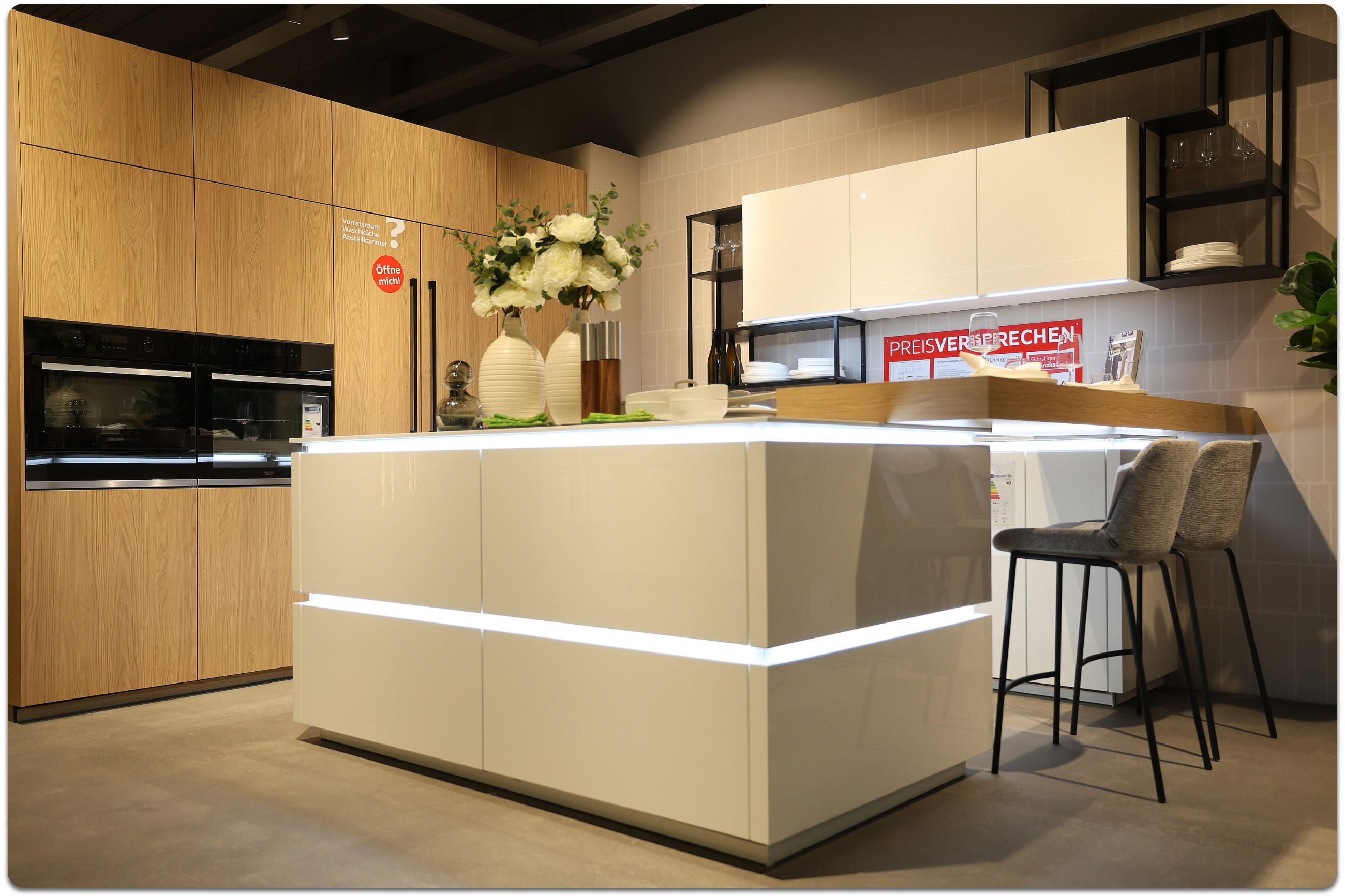 Beige Küche mit LEDs aus der Küchenausstellung Rangsdorf. Rechts befinden sich beige Barhocker an der Küchentheke.