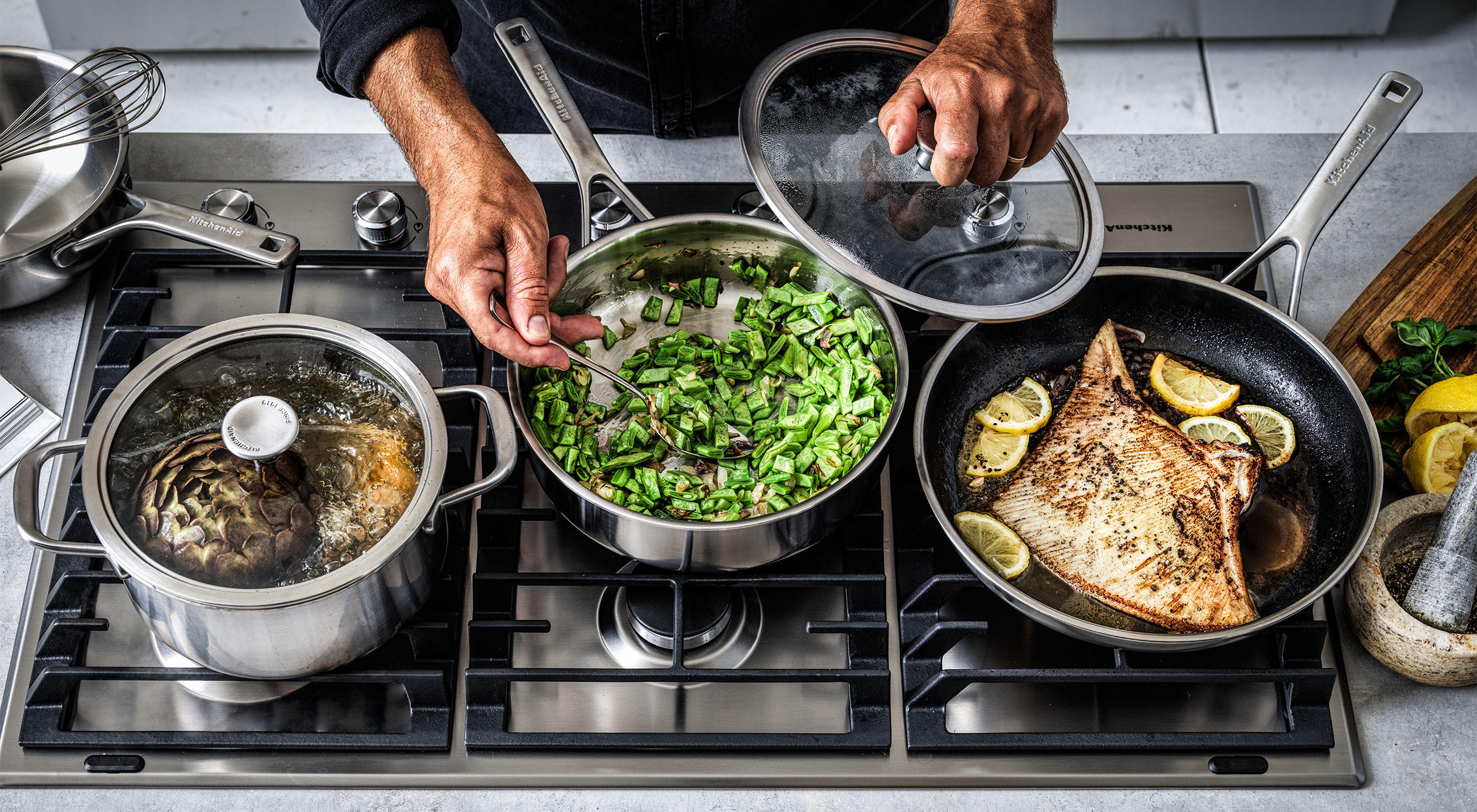 Eine Person kocht am Herd mit Töpfen und Pfannen von KitchenAid.