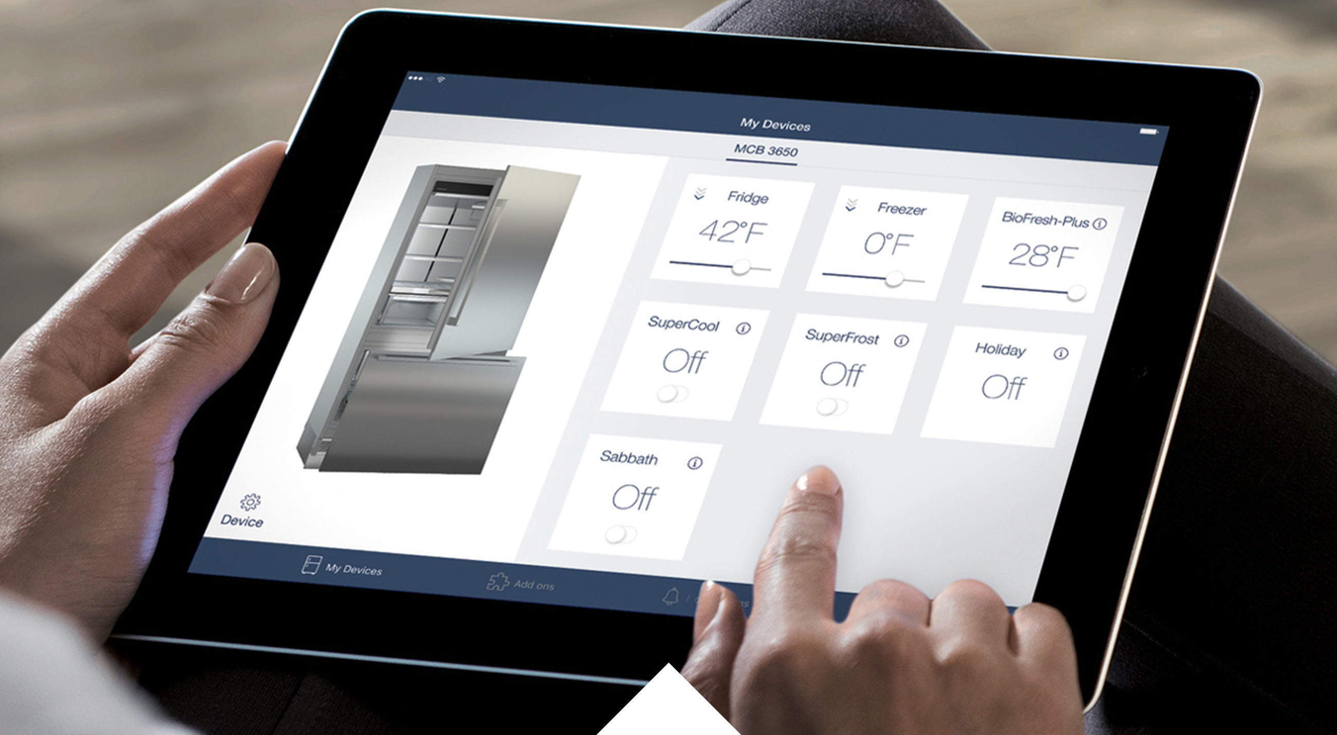 Nahaufnahme von Tablet in den Händen einer Frau, die von dem  Sofa aus ihren Liebherr-Kühlschrank verwaltet, mit Hilfe der Connectivity via SmartDevice-Box.