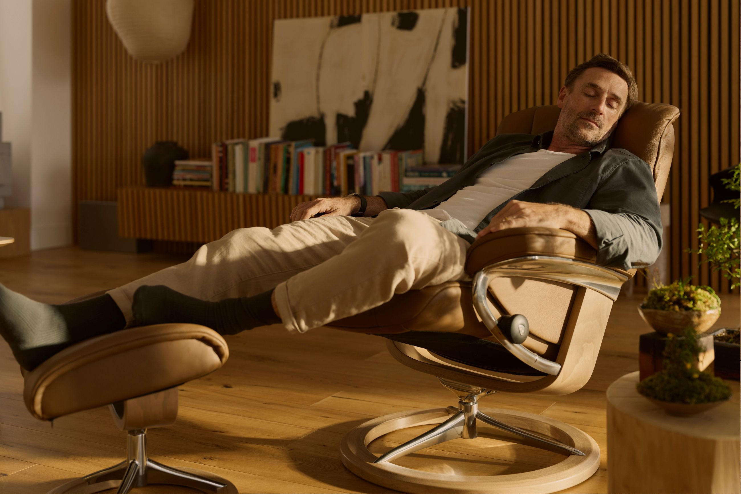 Mann entspannt mit geschlossenen Augen auf einem braunen STRESSLESS Sessel mit Fußhocker.