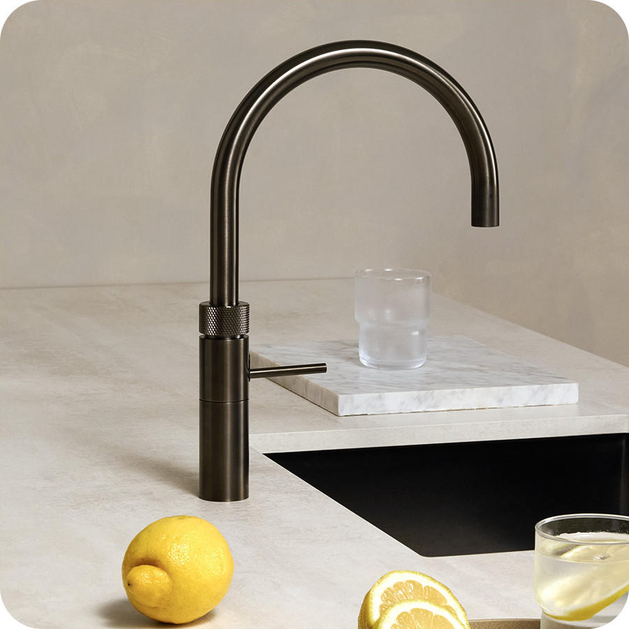 QUOOKER Classic Fusion Gun Armatur in dunklem Metallfinish mit hohem, gebogenem Auslauf über einer schwarzen Spüle; auf der Arbeitsplatte liegen Zitrone und Zitronenscheiben, daneben steht ein Glas Zitronenwasser.