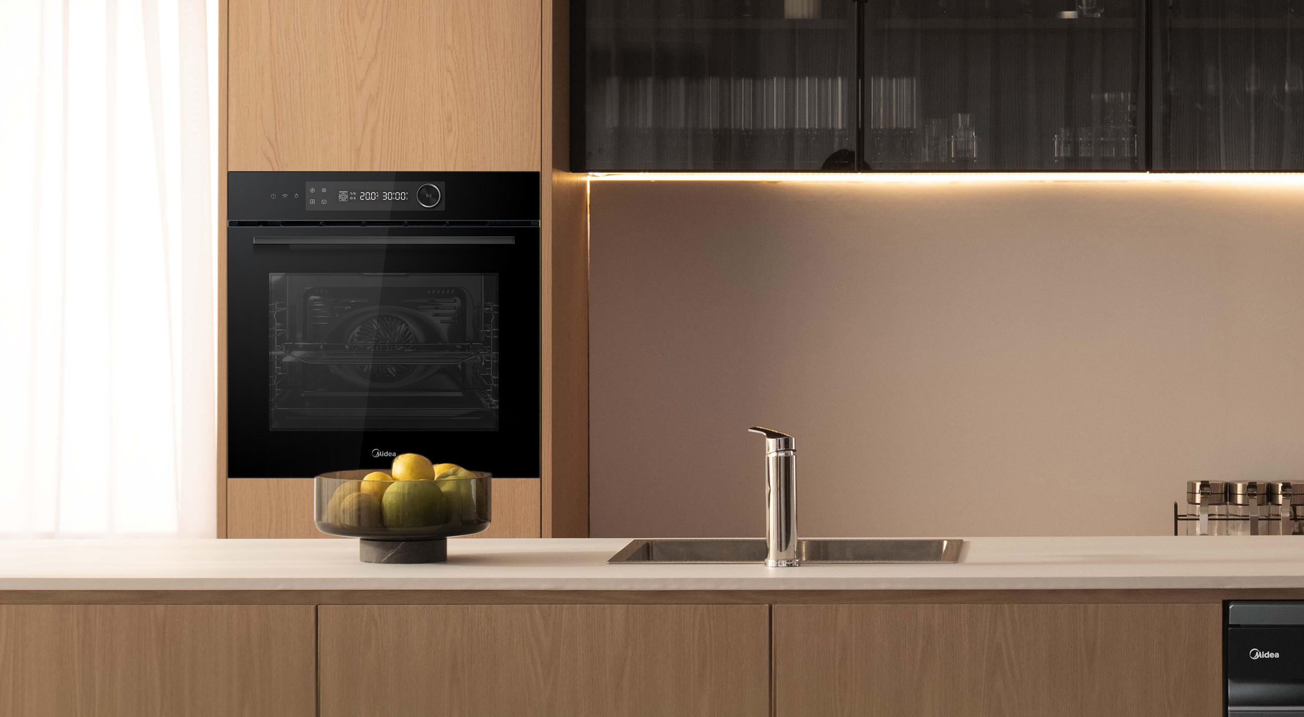 Integrierter Midea Backofen in einer modernen Küchenzeile mit Holzfronten; davor Arbeitsplatte mit Spüle und Obstschale, indirekte Beleuchtung im Hintergrund.