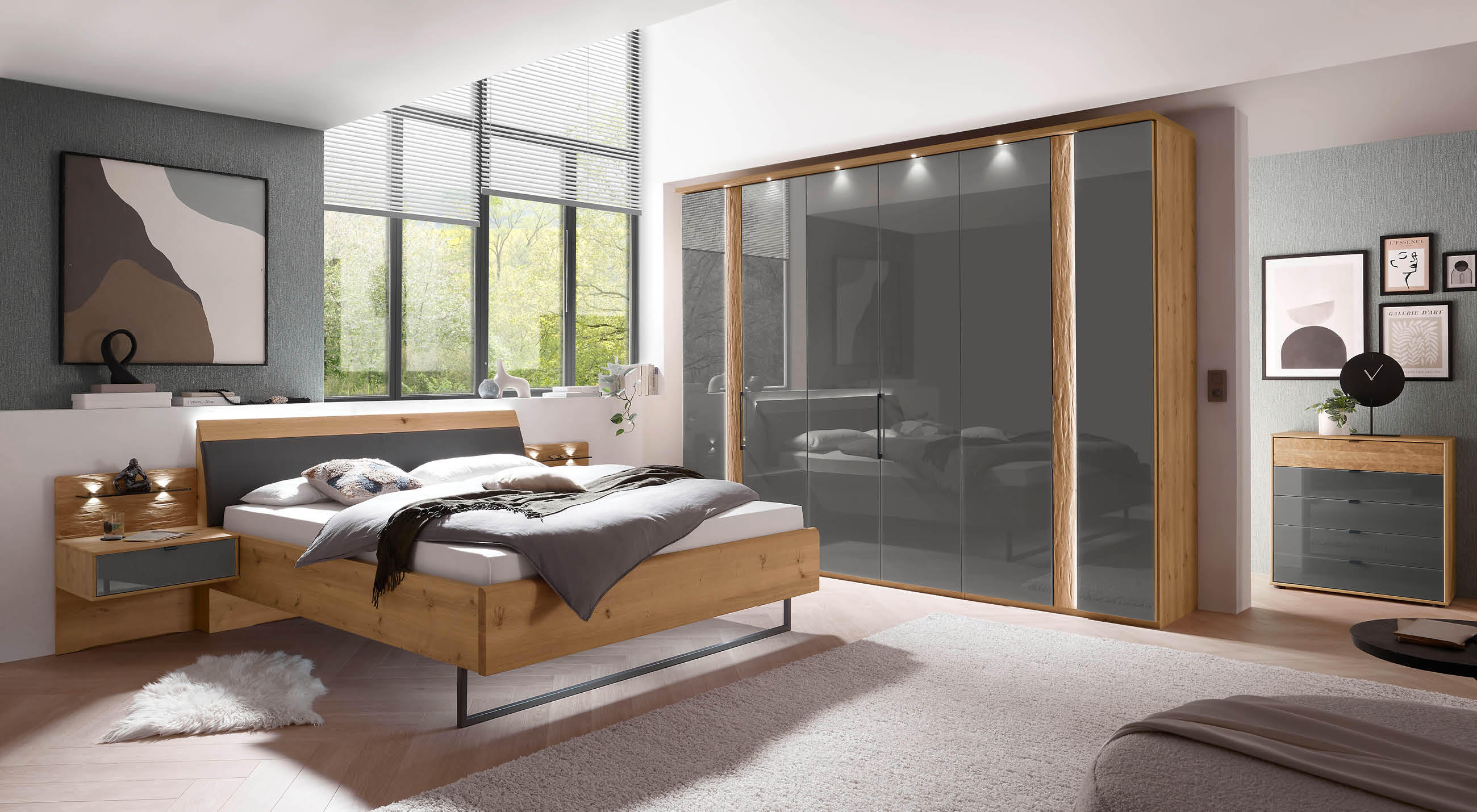 Ein Schlafzimmer mit einem Bett, einer Kommode, Kleiderschrank in der Farbe Anthrazit und einem Fenster, das Tageslicht hereinlässt.