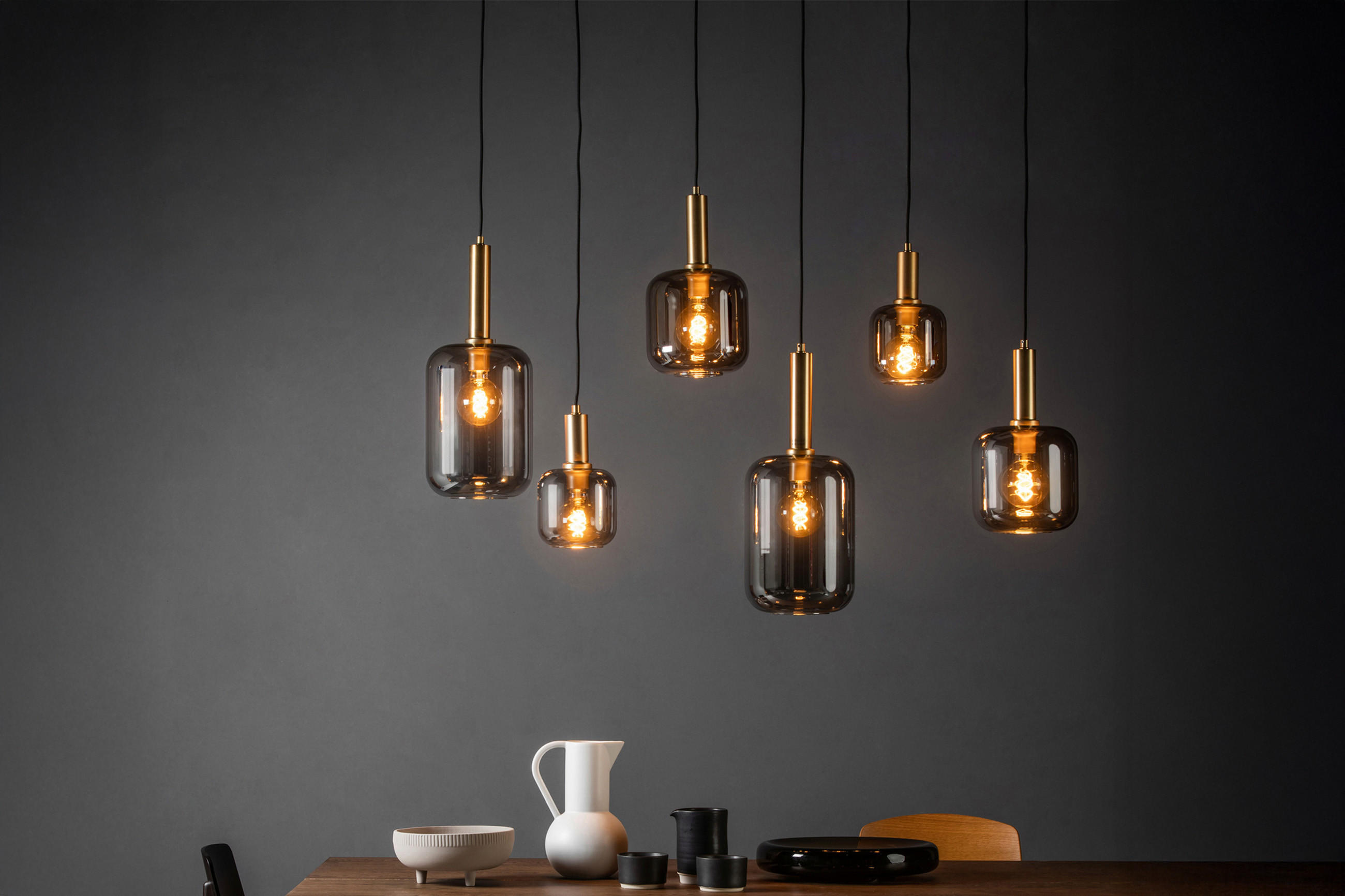 Sechs goldenen Pendelleuchten und schlichtem Geschirr vor dunkler Wand.
