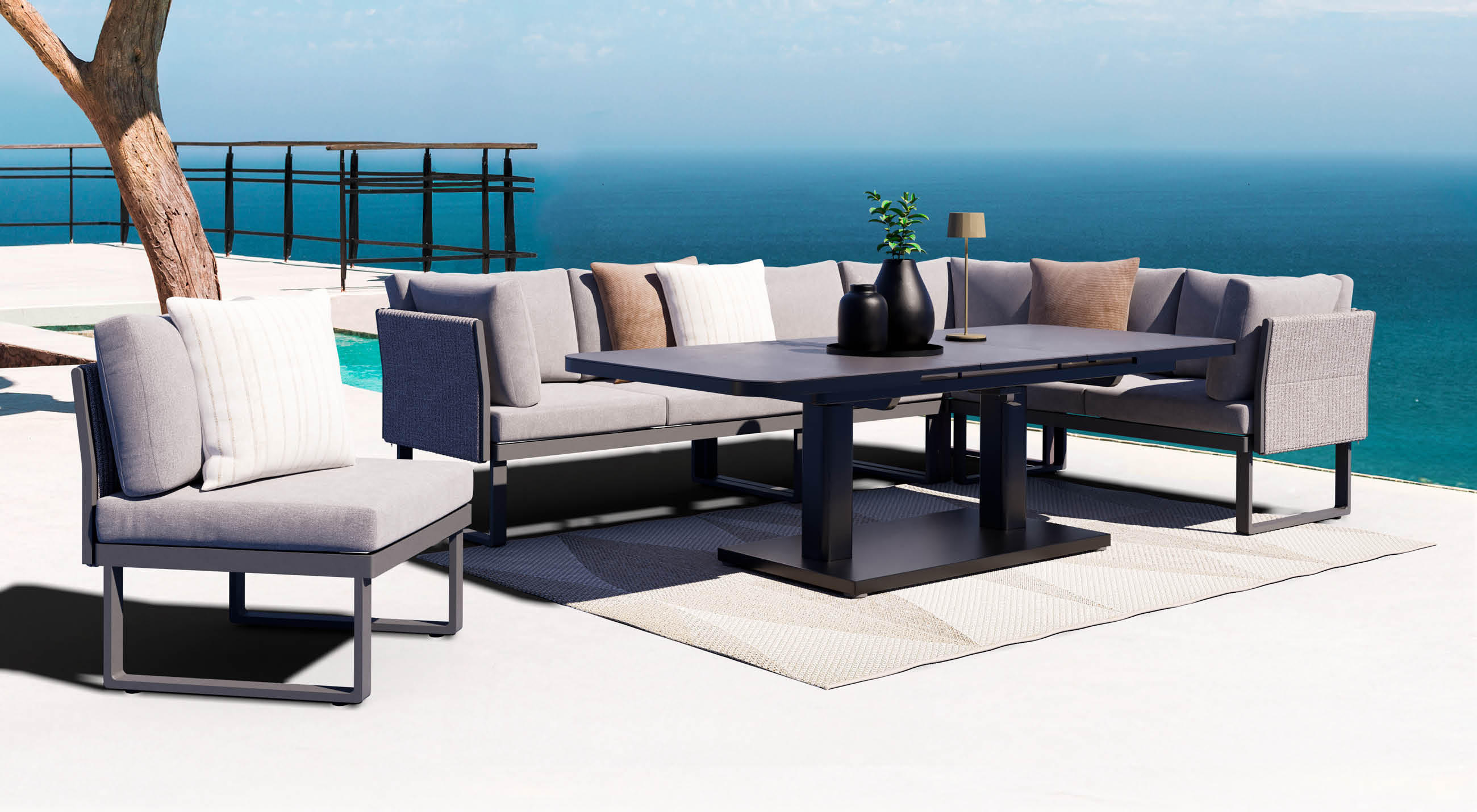 Graue Outdoor-Sitzgruppe mit Ecksofa und großem Tisch auf heller Terrasse am Pool, im Hintergrund weiter Meerblick.