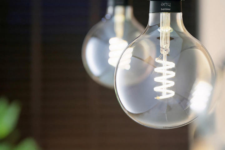 Zwei runde Philips Hue Glühbirnen mit sichtbaren Spiralfilamenten hängen an schwarzen Fassungen, im Hintergrund ist eine grüne Pflanze zu sehen