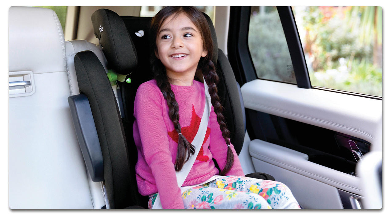 Mädchen mit rosanem Pullover in einem schwarzen Kindersitz im auto