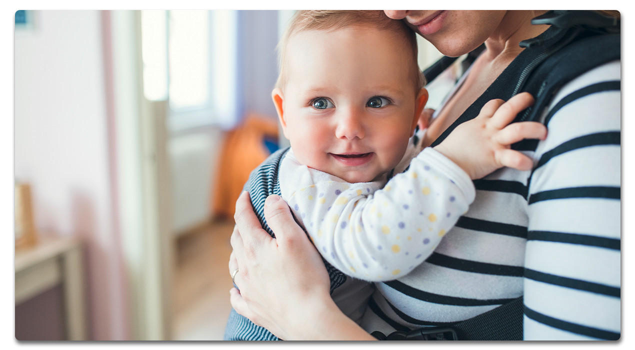 Frau mit Baby in Trage zuhause