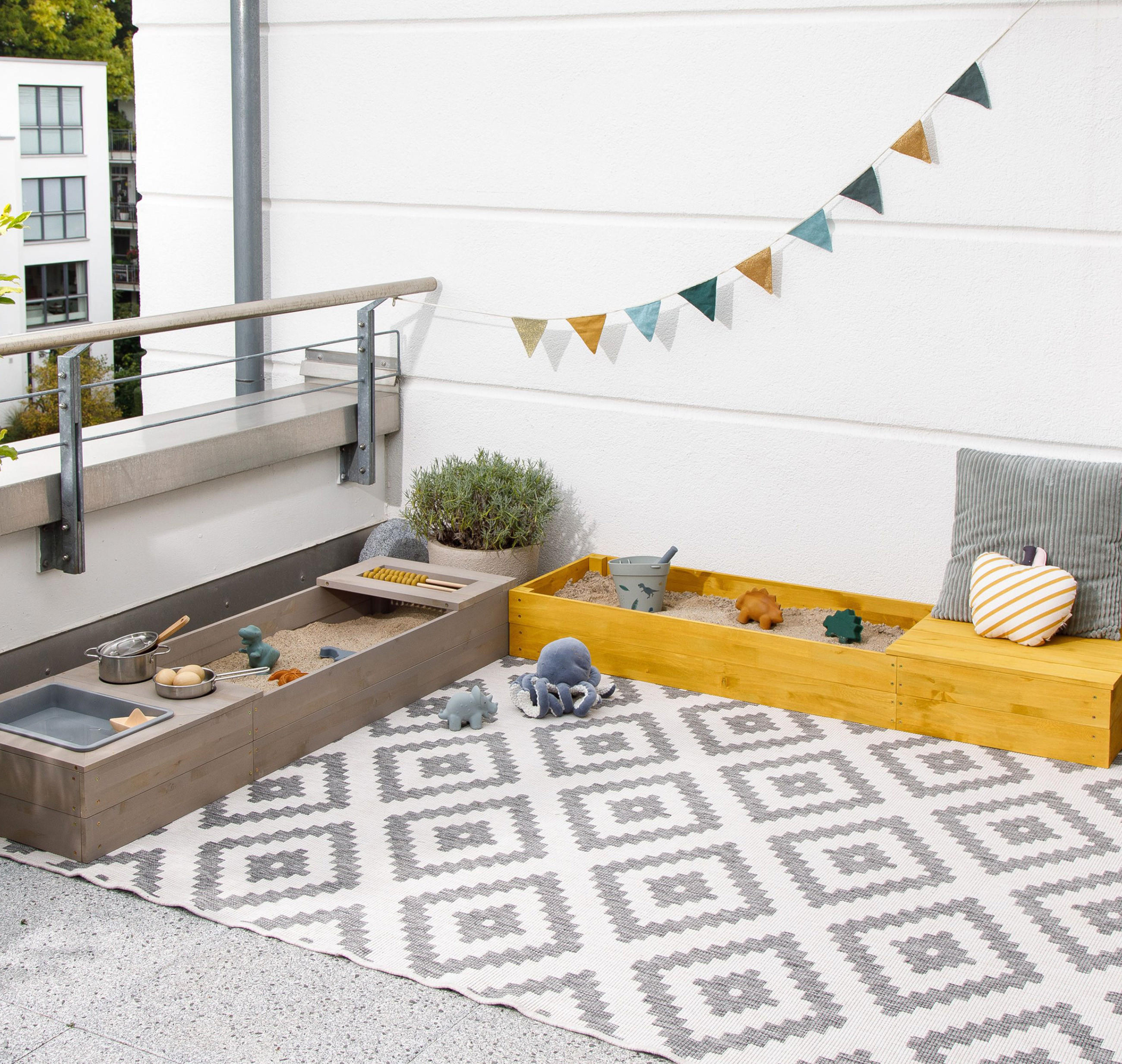 Balkon mit hellgrauen Outdoorteppich mit zwei Sandkästen