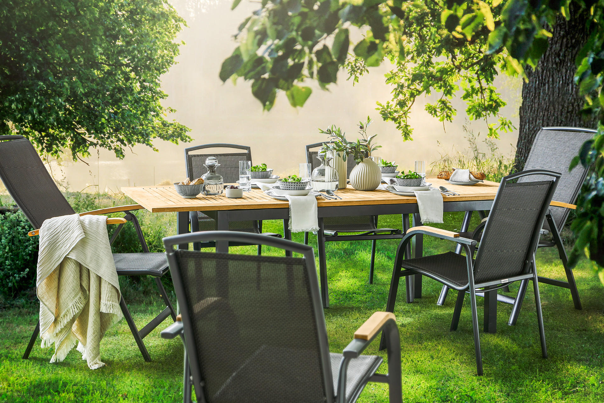 Gartentisch und Gartenstühle stehen in einem sonnigen und grün bepflanzten Garten