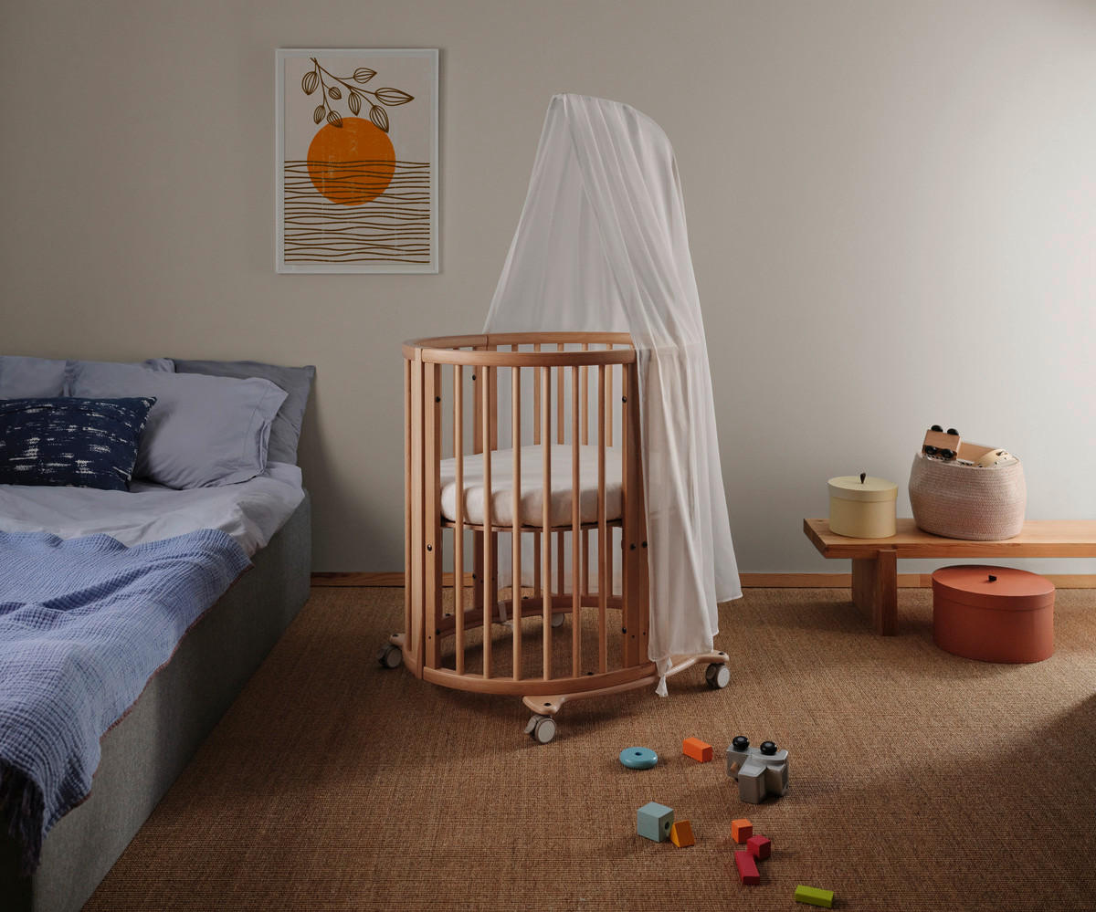 Ein rundes Gitterbett aus Holz mit einem weißen Tuch darüber