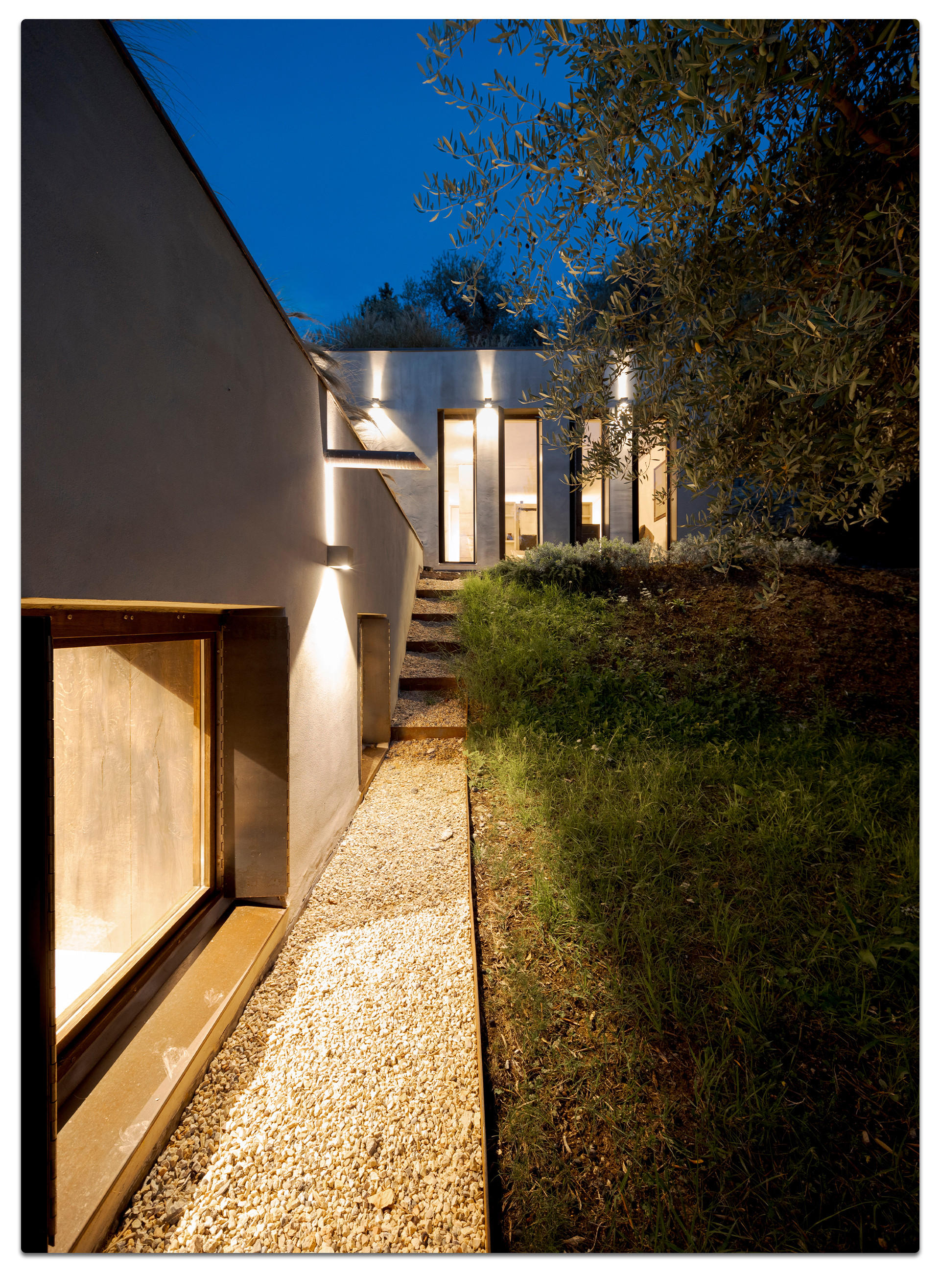 Modernes Haus mit beleuchtetem Weg und großen Fenstern bei Nacht.