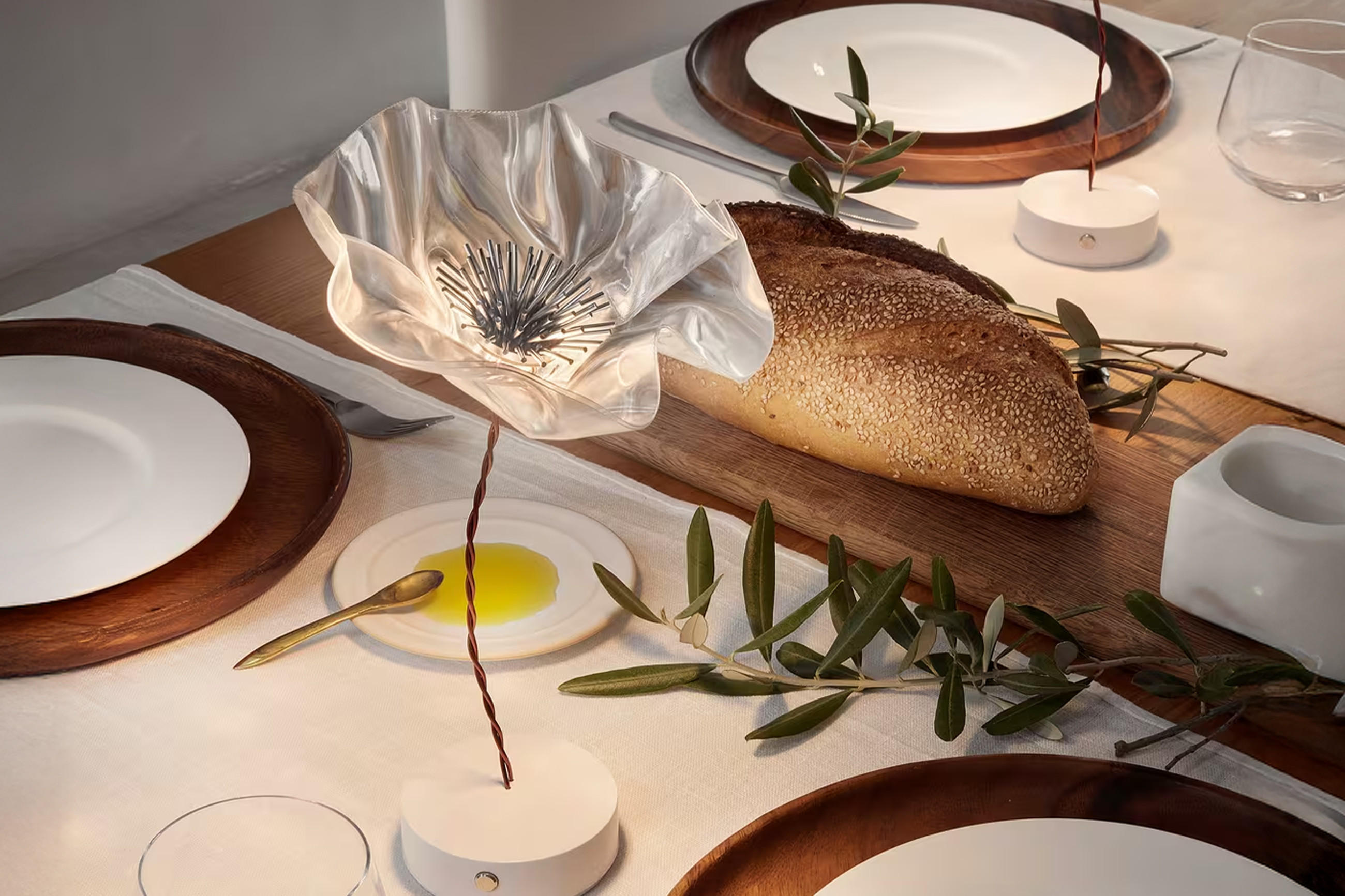 Gedeckter Esstisch mit weißer Tischdecke und dekorativer Blumen-Tischleuchte.