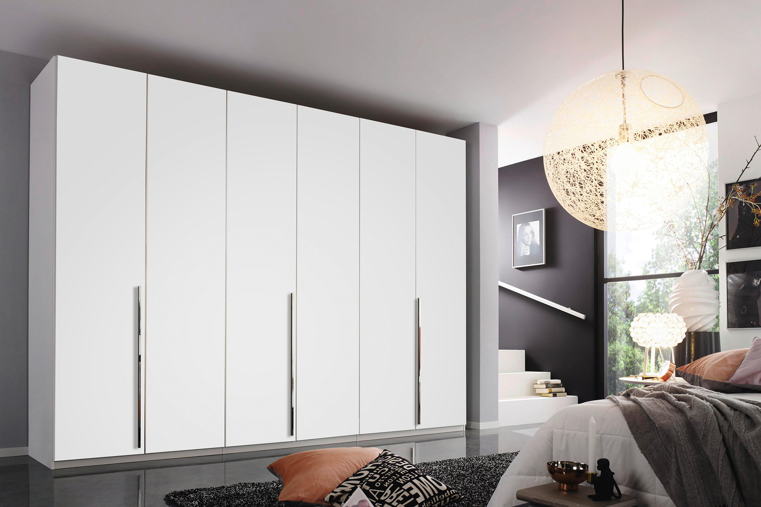 Großer weißer Kleiderschrank mit mehreren Türen und langen Griffen in modernem Schlafzimmer; rechts Bett, Teppich und große Fensterfront mit Lampe.