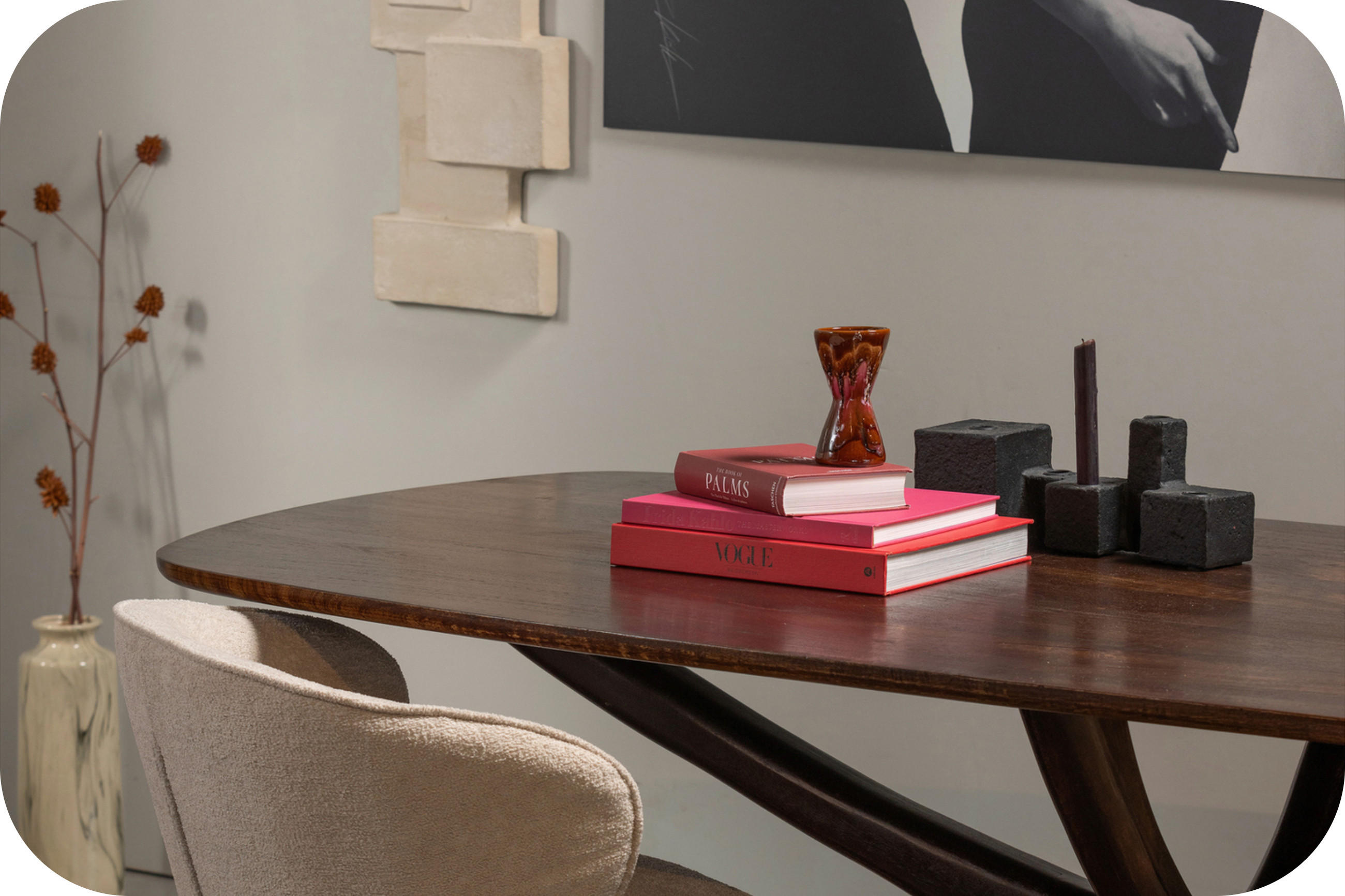 Detailaufnahme eines modernen Essbereichs mit dunklem Holztisch, Polsterstuhl und Deko (Bücher, Kerzenhalter, Vase).