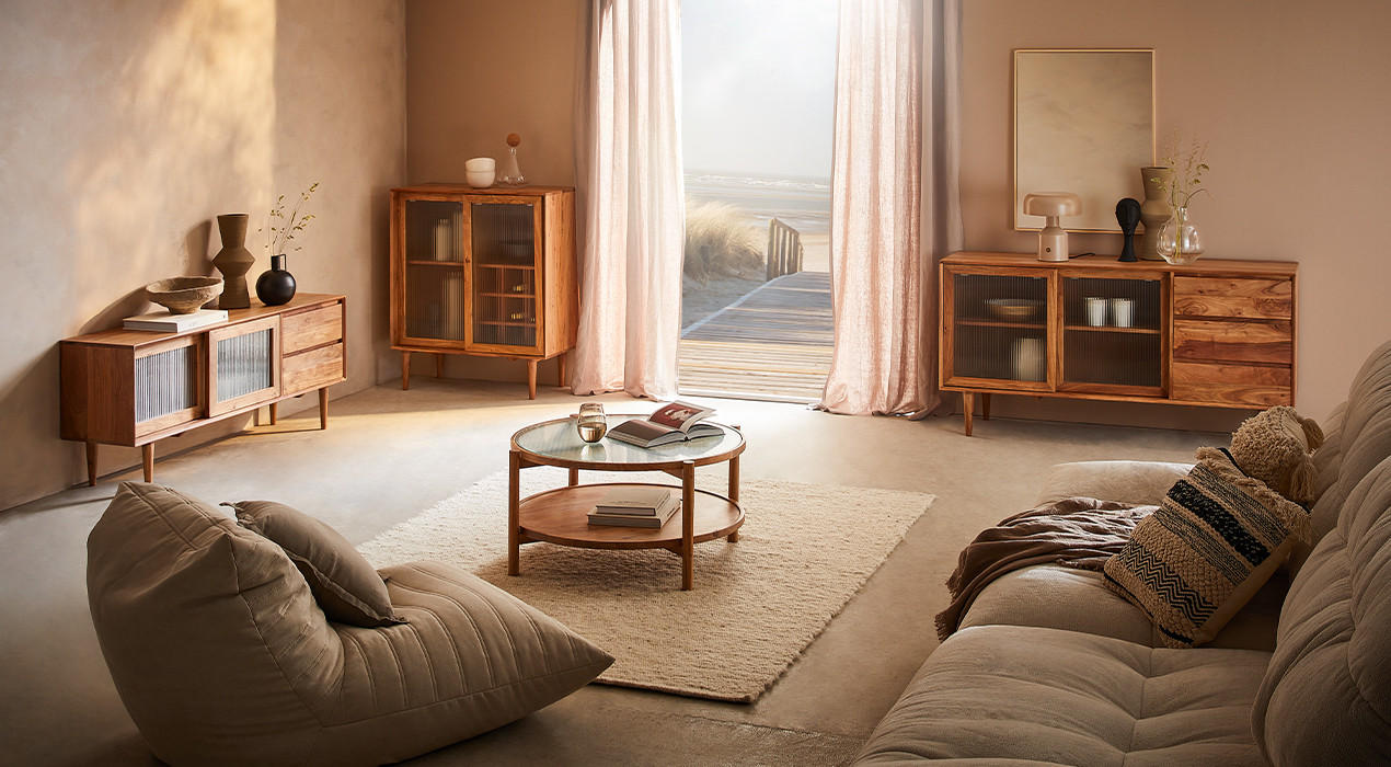 Gemütliches Wohnzimmer mit Möbeln aus Holz und warmen Farbtönen, darunter ein Sideboard, Couchtisch und Sessel. Dekoriert mit Vasen und Textilien, ideal für eine entspannte Atmosphäre