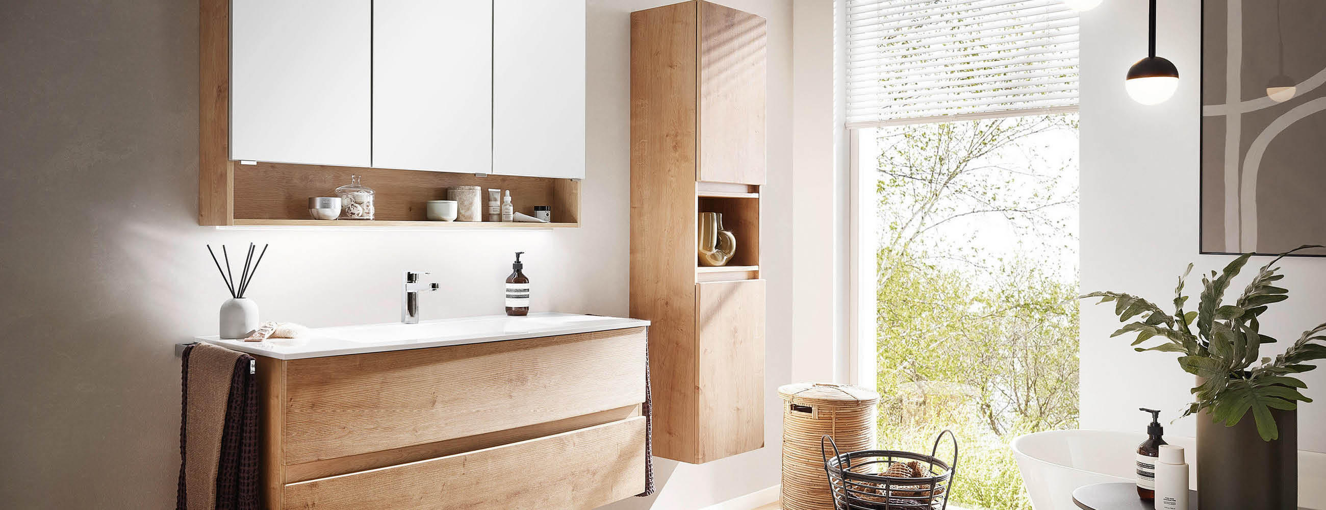 Modernes Badezimmer mit Holzwaschtisch, großem Spiegel, freistehender Badewanne und Fenster mit Blick ins Grüne