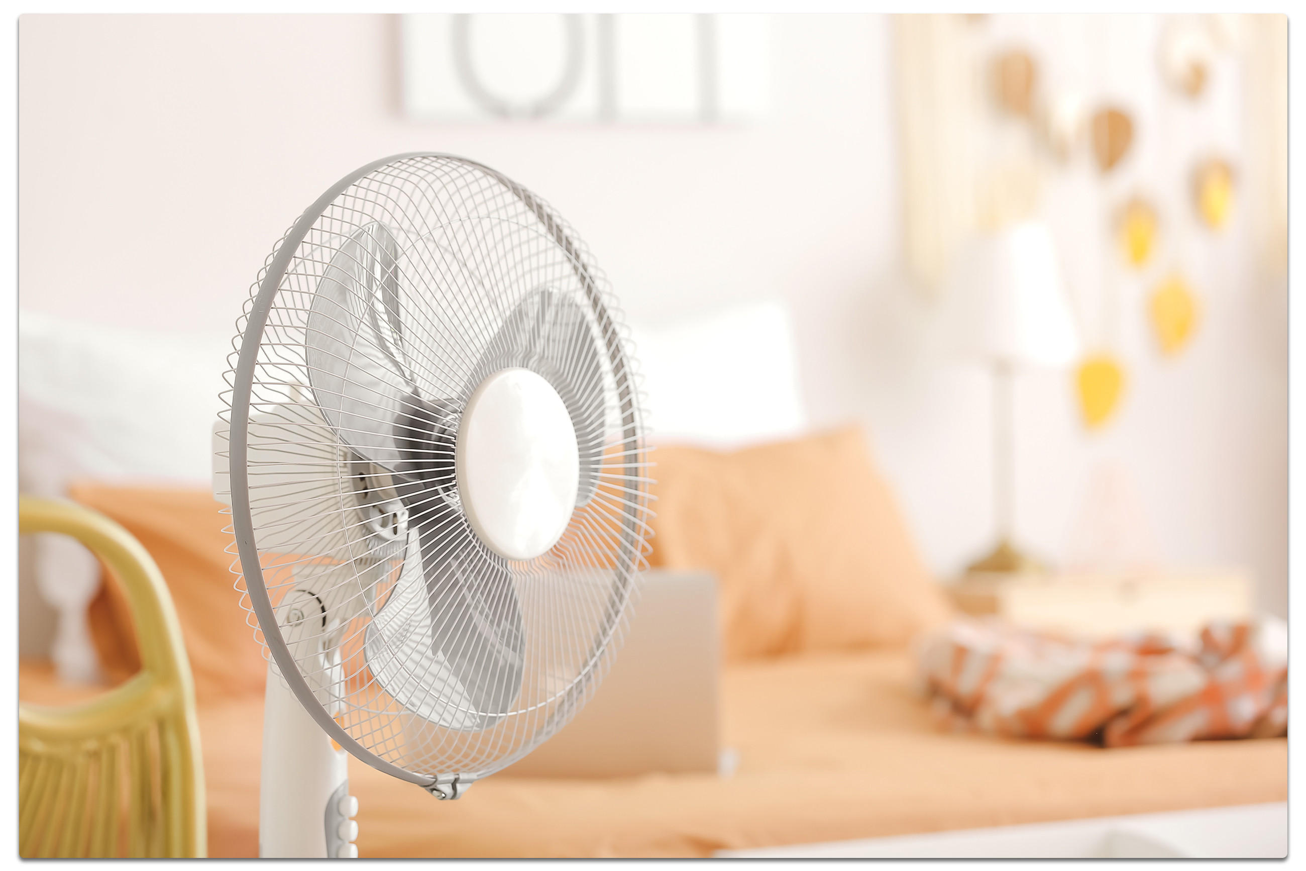 Ventilator vor Bett mit orangefarbener Bettwäsche.