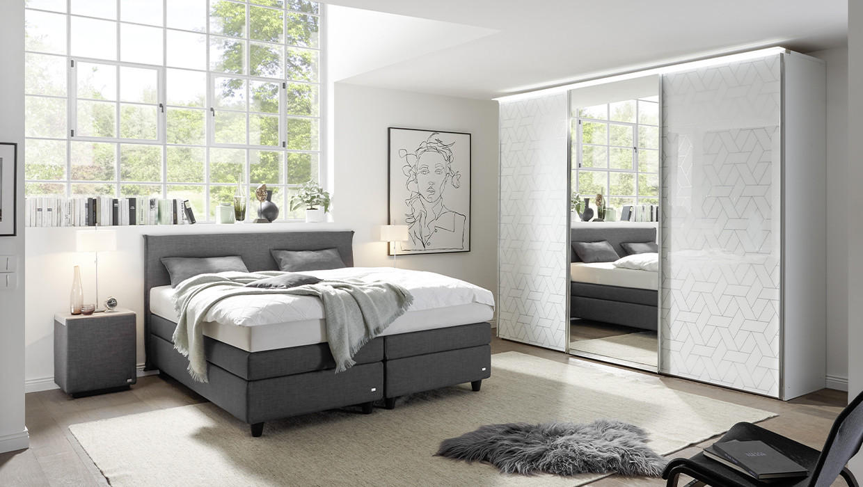 moderne zariadená spálna, posteľ boxspring, skriňa s posuvnými dverami a zrkadlom, kožušina, obraz na stene