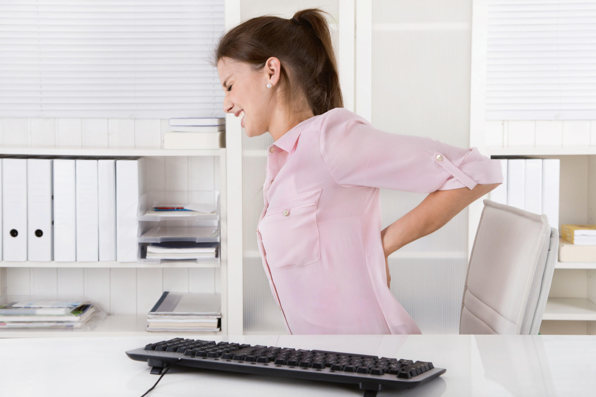 Frau mit RÃ¼ckenschmerzen am Arbeitsplatz