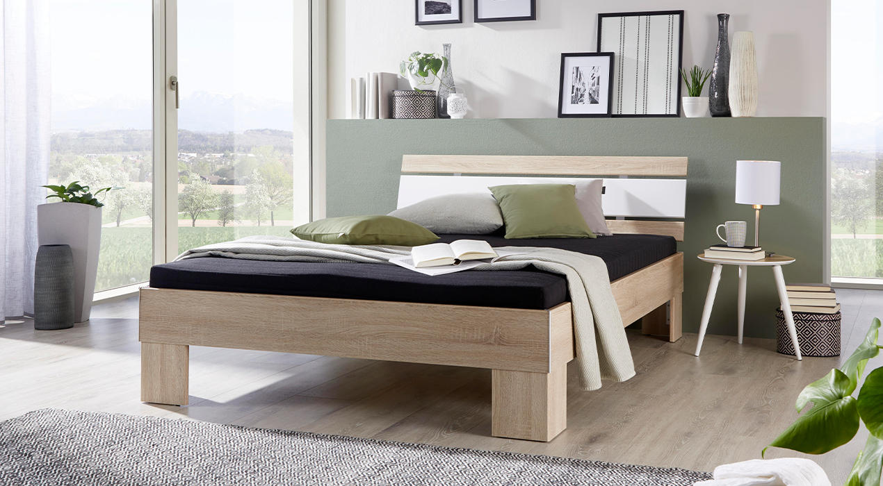 Helles Futonbett mit weißem Element im Kopfteil.