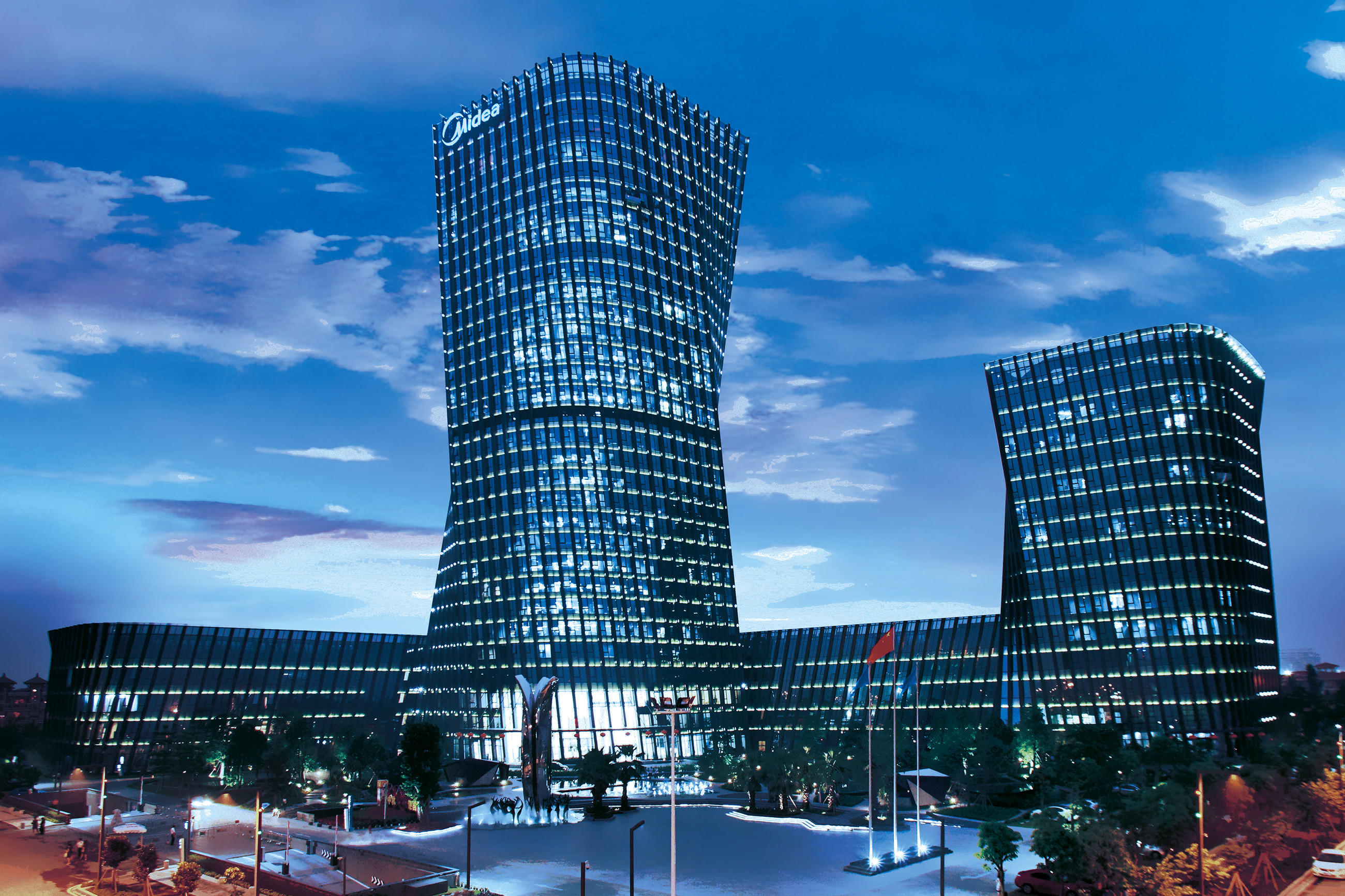 Beleuchtetes Midea-Hochhausensemble bei Dämmerung vor blauem Himmel; modernes Firmengebäude als Symbol für globale Präsenz und Innovation.