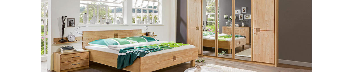 Einblick in ein Schlafzimmer mit Bett, Kommode und Kleiderschrank mit Spiegel.